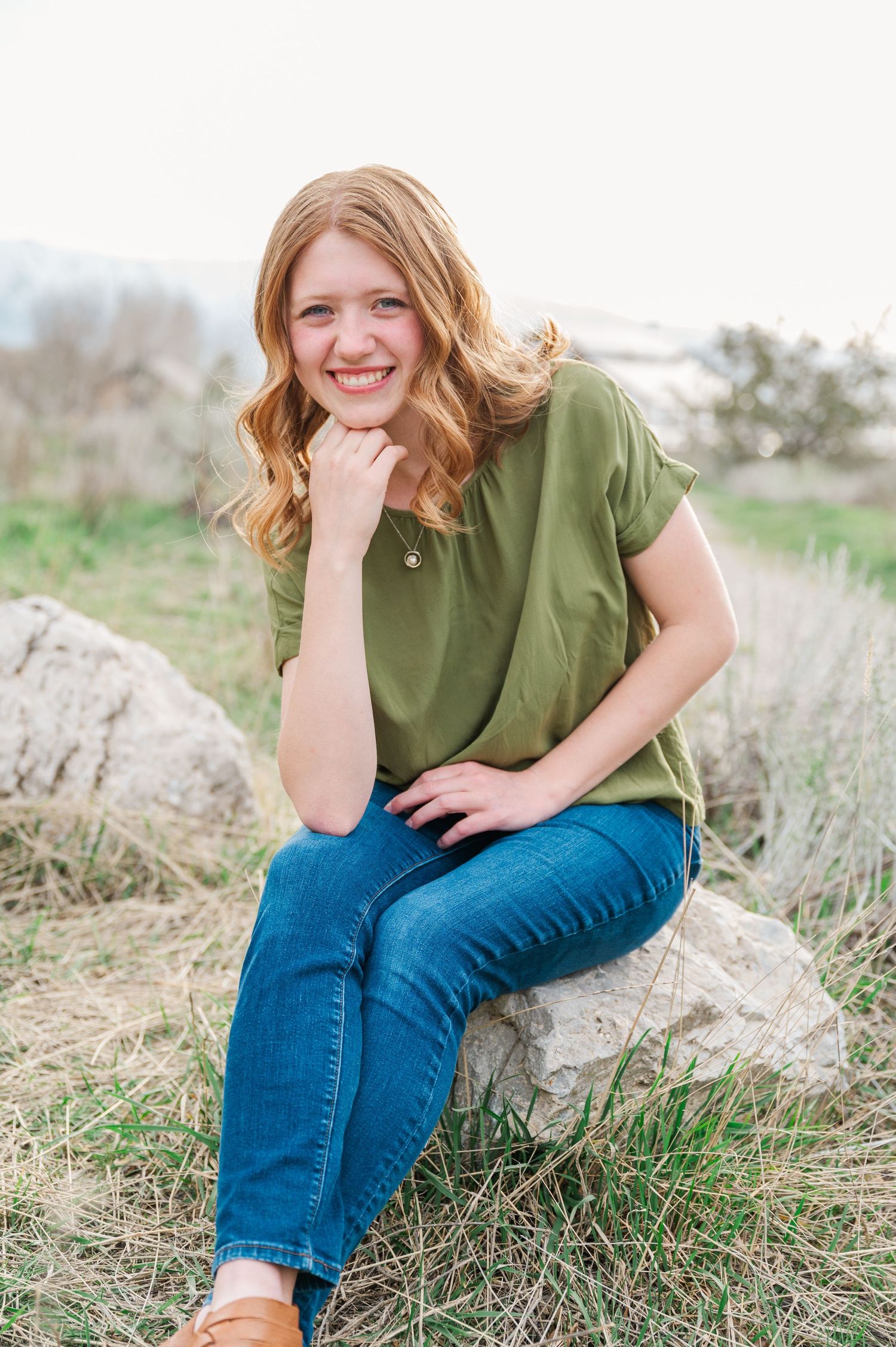 Casual portrait of someone sitting on a rock wearing olive green top and jeans.
