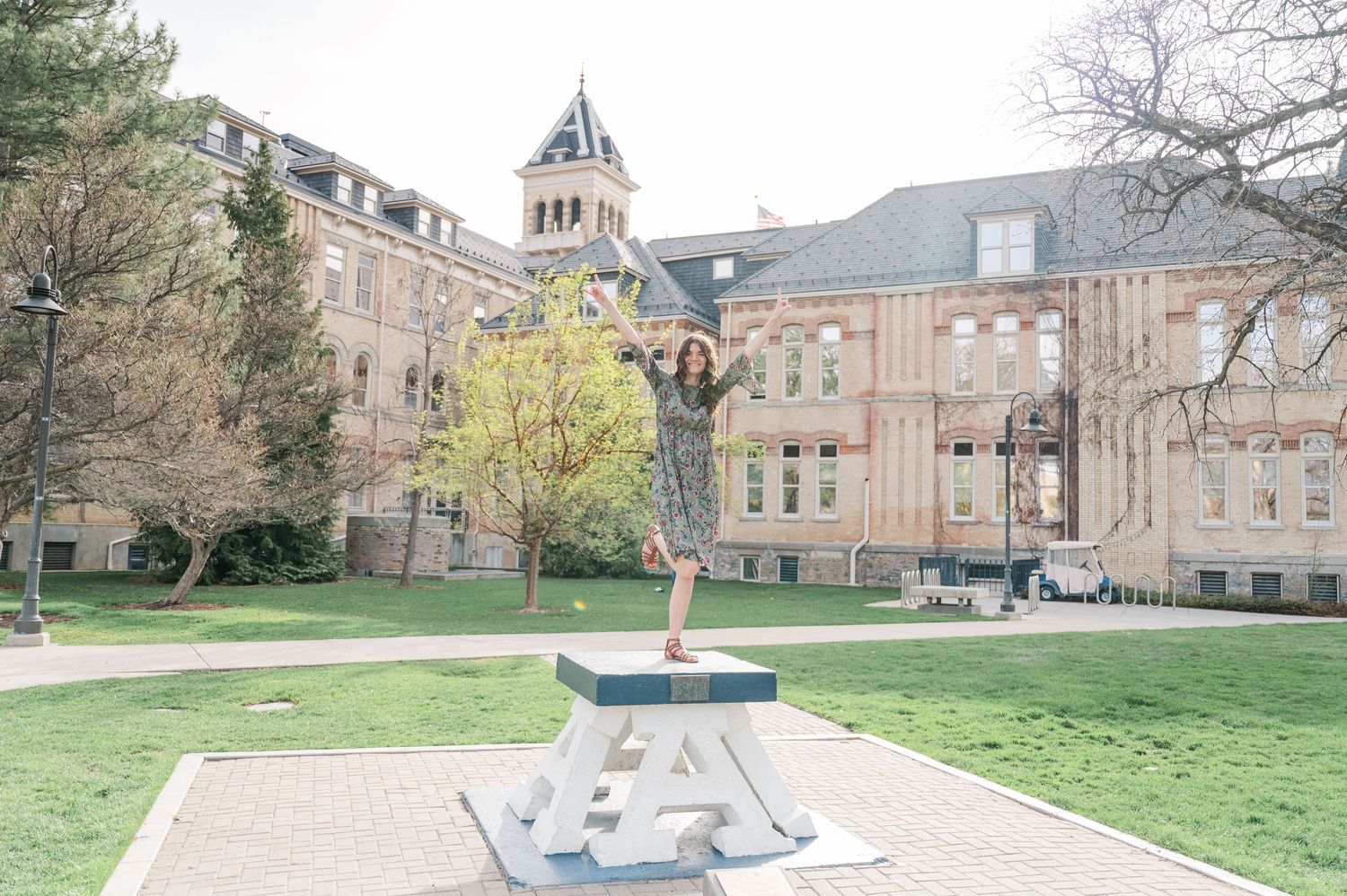 Statue and historic university building with Gothic architecture and clock tower on a grassy lawn.