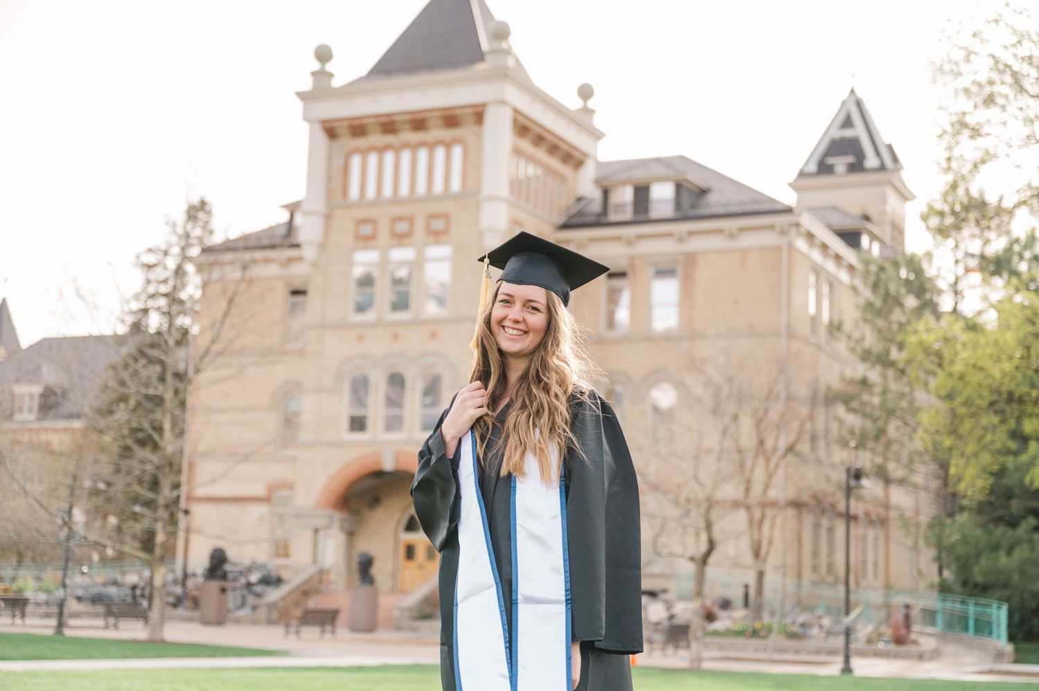 Graduate in cap and gown standing in front of historic university building.