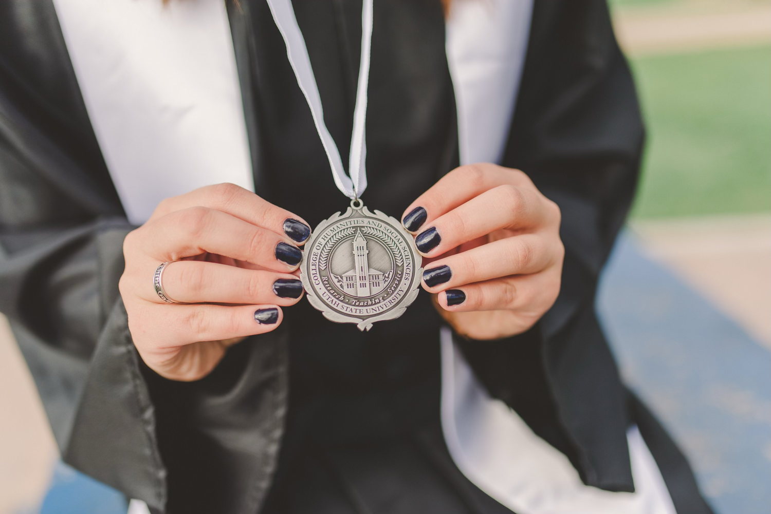 Hands holding a graduation medal or academic achievement award against black graduation gown.