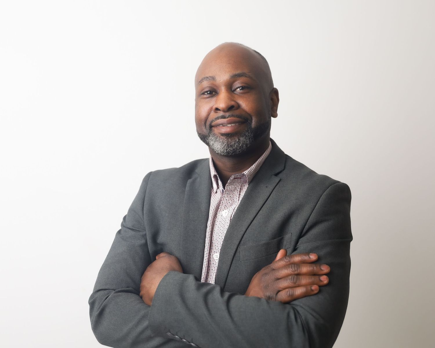 Professional in grey suit with crossed arms against white background.