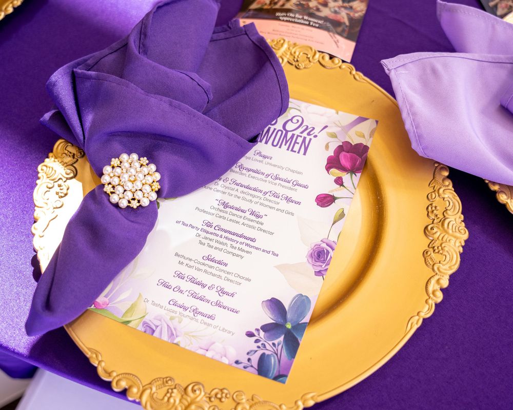 Ornate place setting with purple napkin and gold charger plate featuring an event menu.