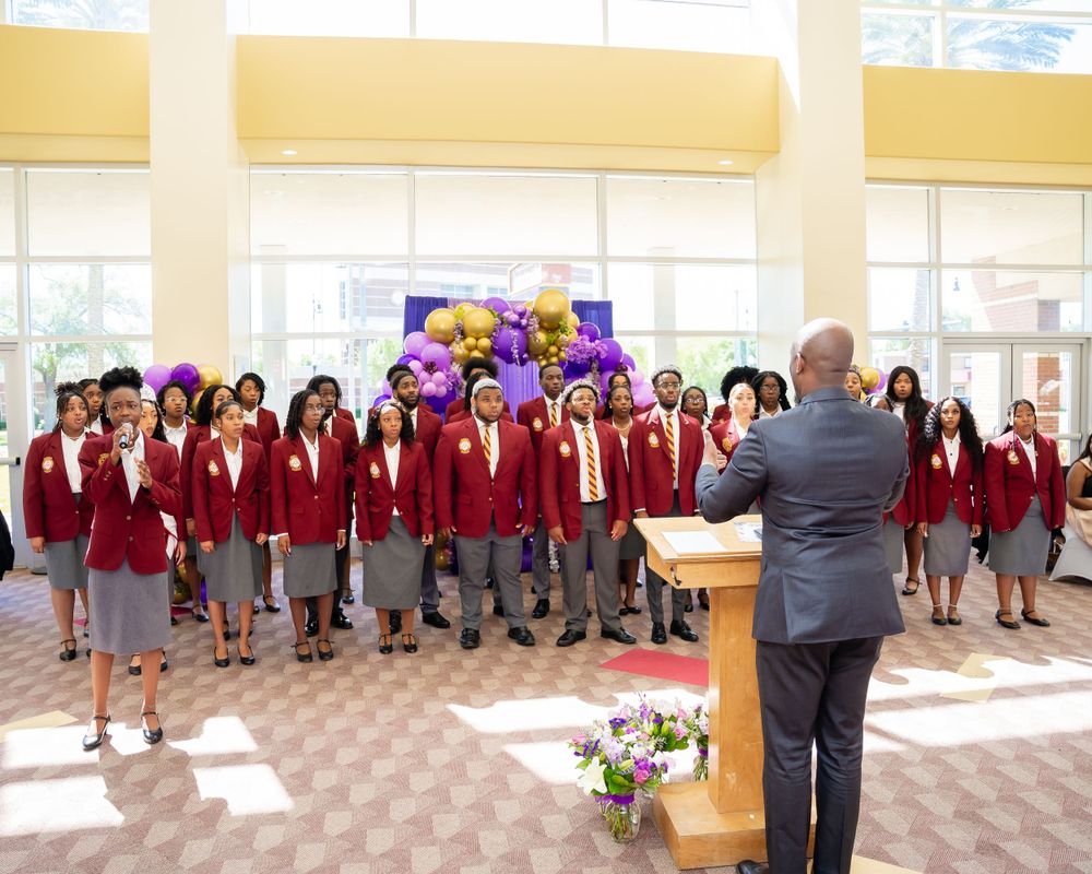 Choir group in red robes performing in front of purple and gold balloon decorations.