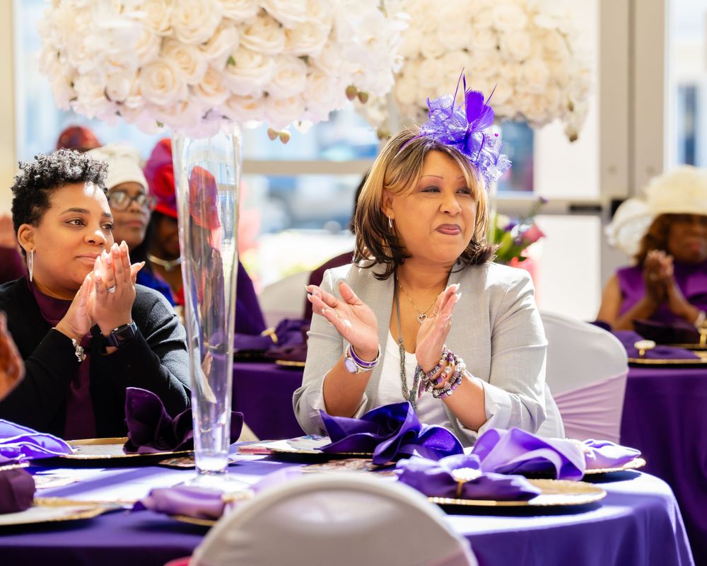 Event guest wearing purple fascinators at decorated table with purple and white decor.
