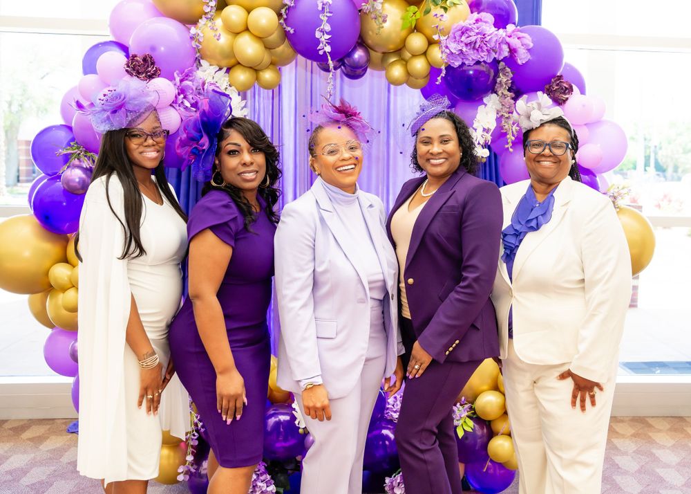 Group photo with purple and gold balloon arch backdrop at formal event.