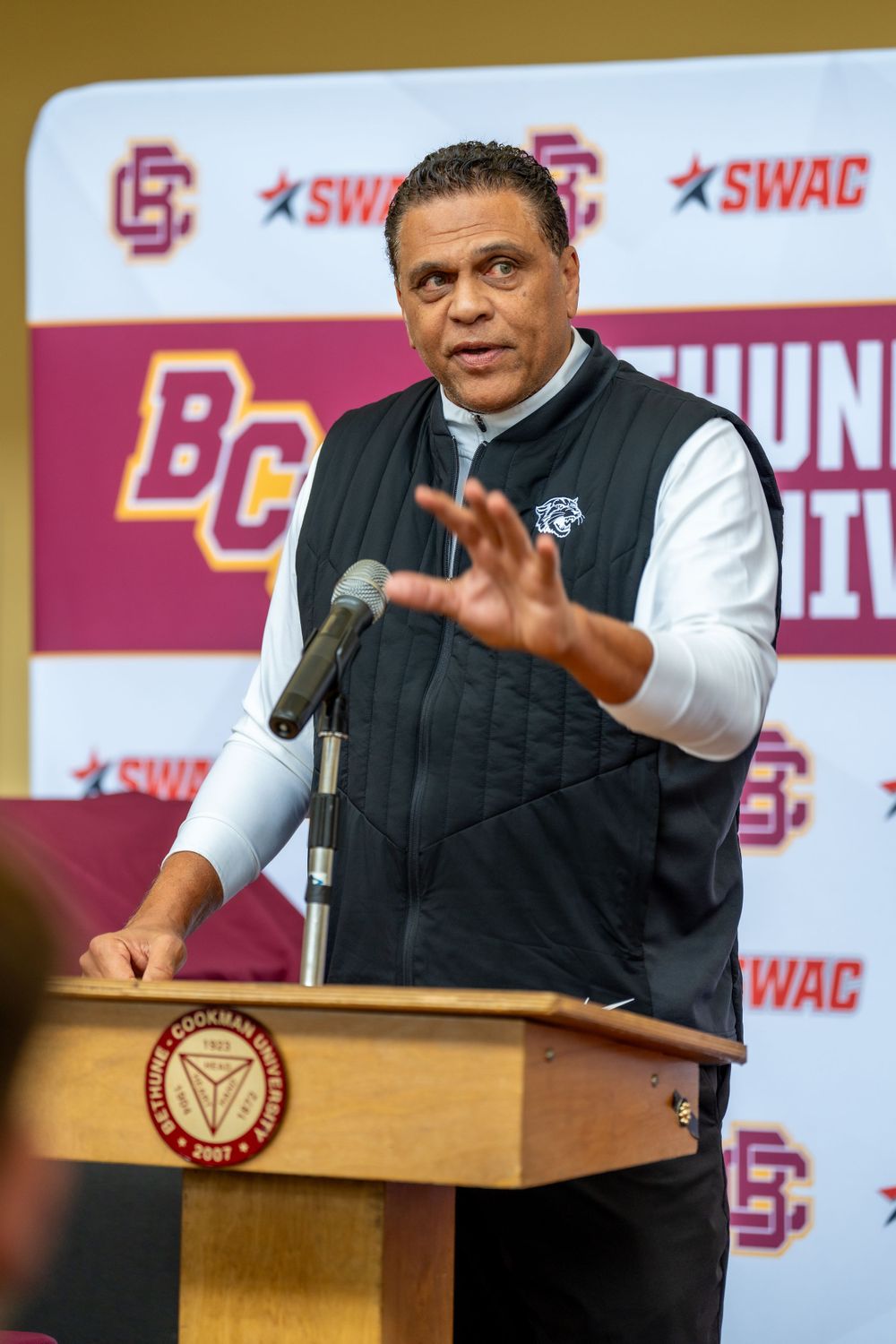 Speaker gestures while addressing audience at university branded podium.