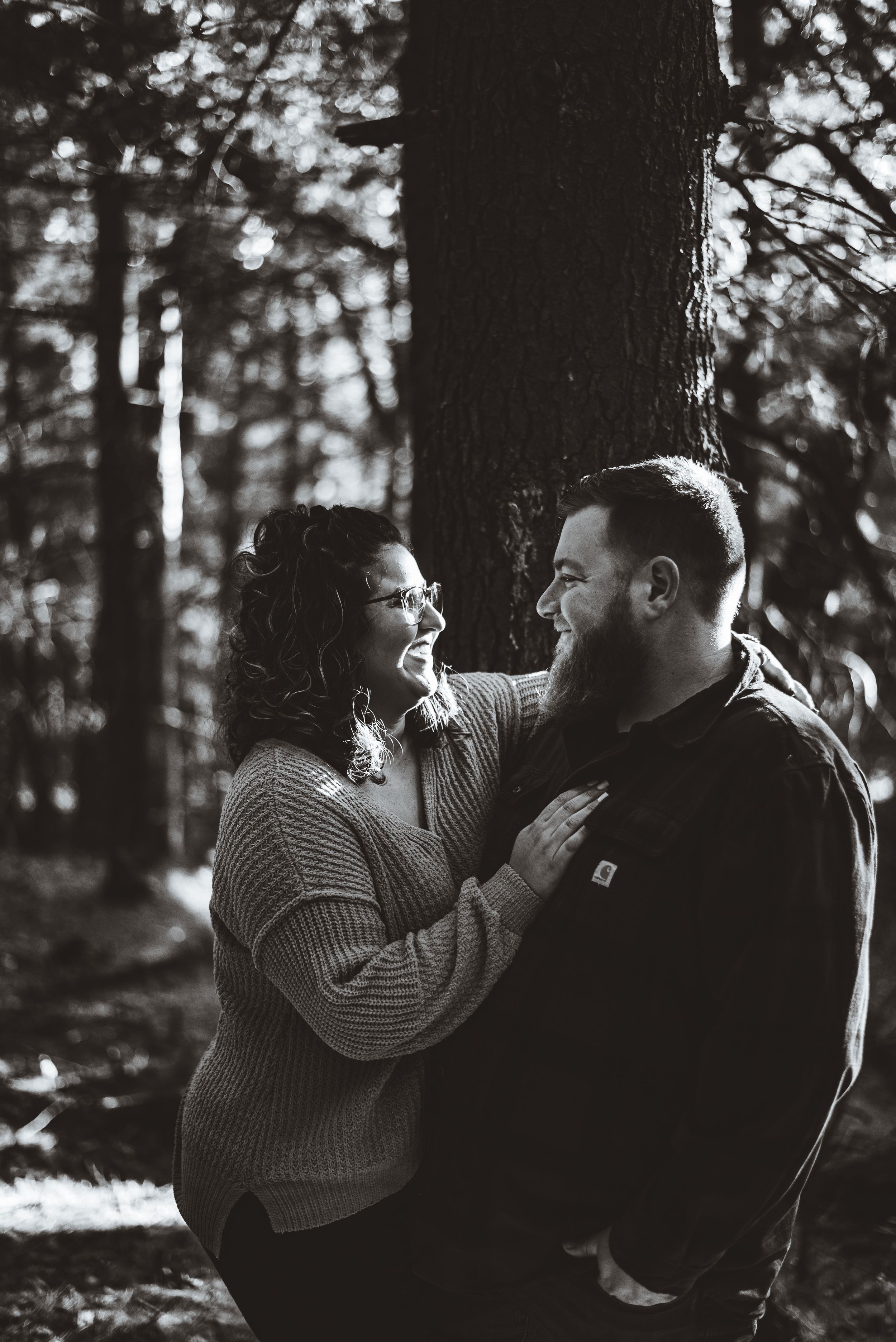 Black and white portrait of couple sharing intimate embrace against forest backdrop.