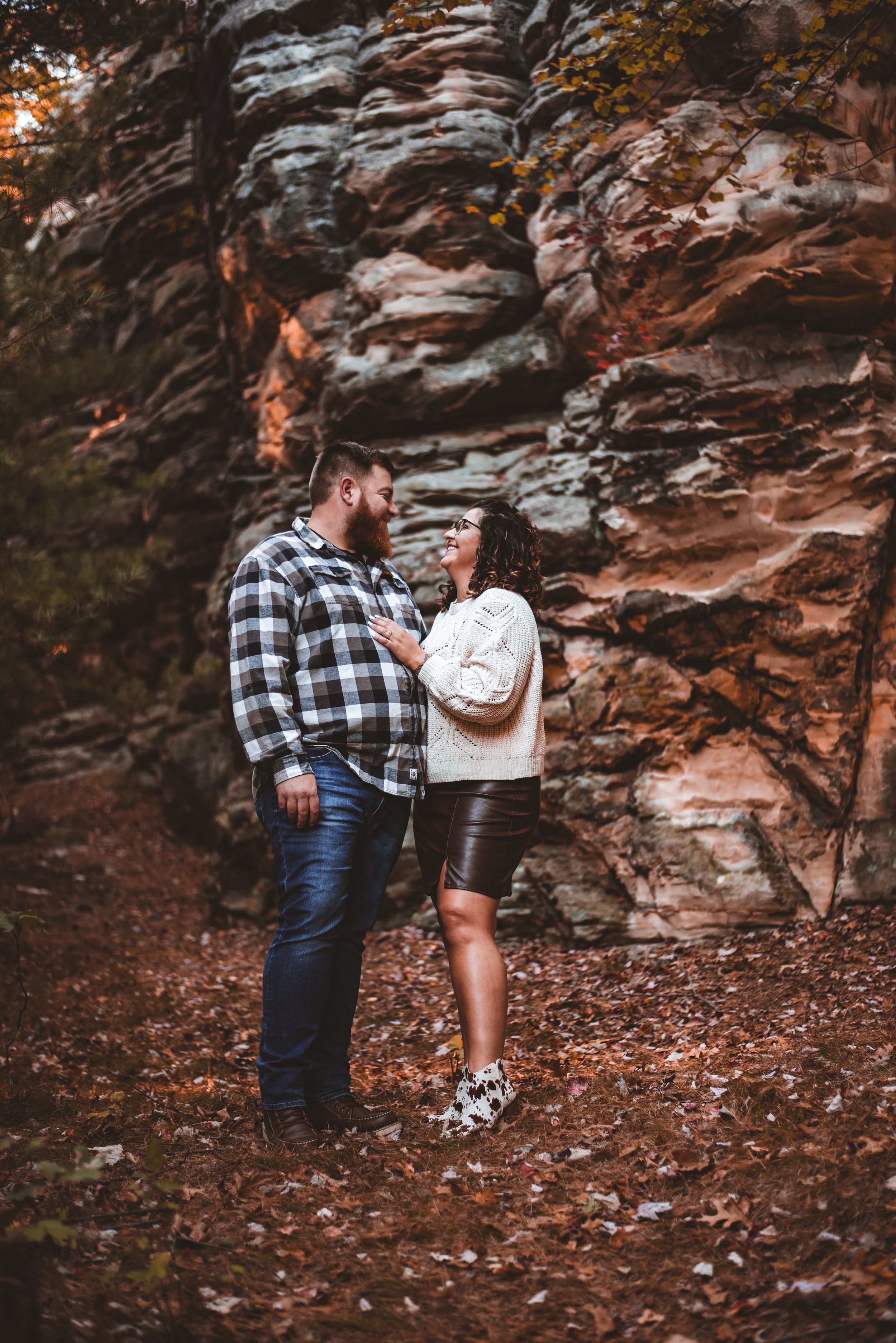 Couple sharing an intimate moment against dramatic rocky cliff backdrop covered in fall leaves.