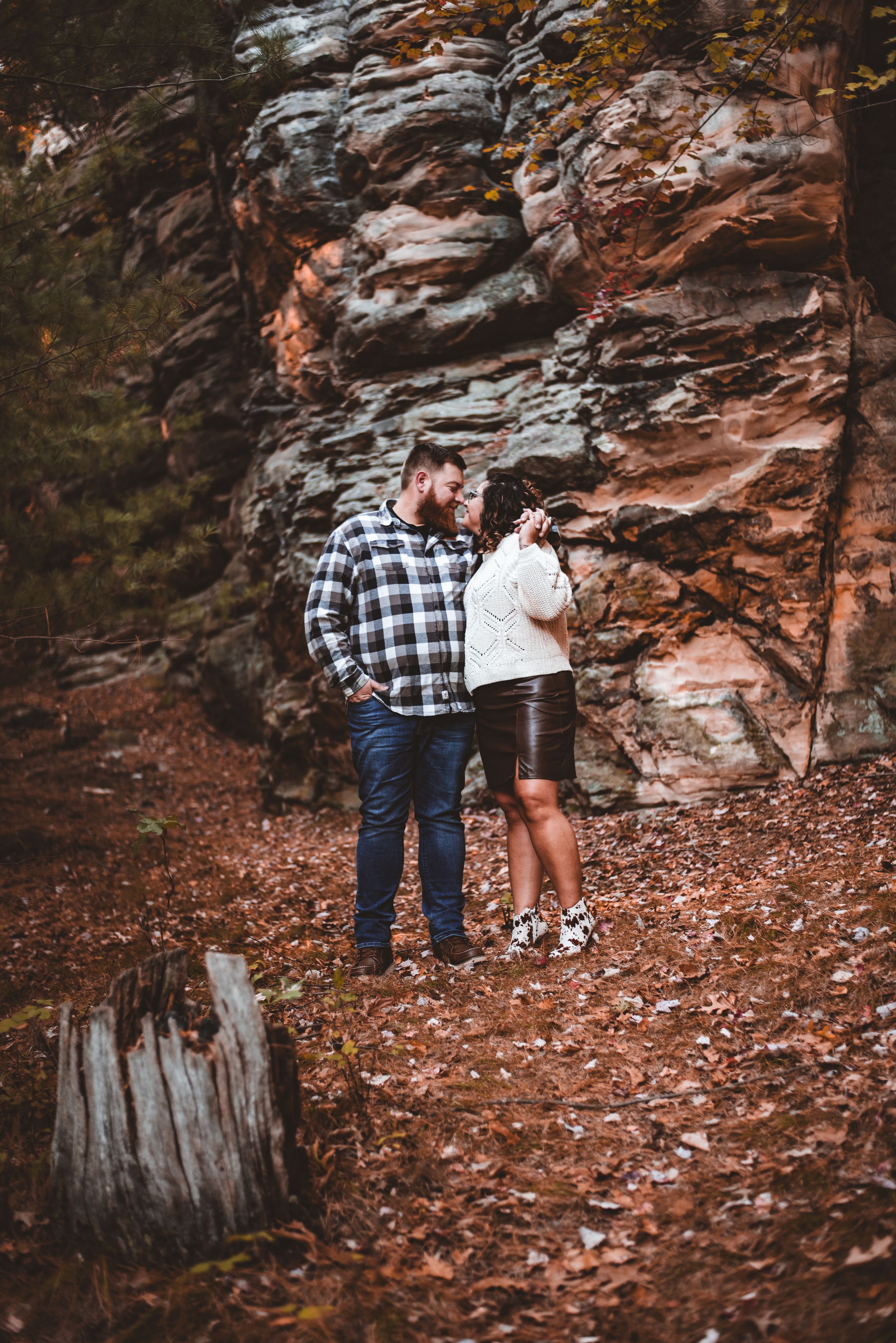A couple stands together near towering rock formations on an autumn trail.