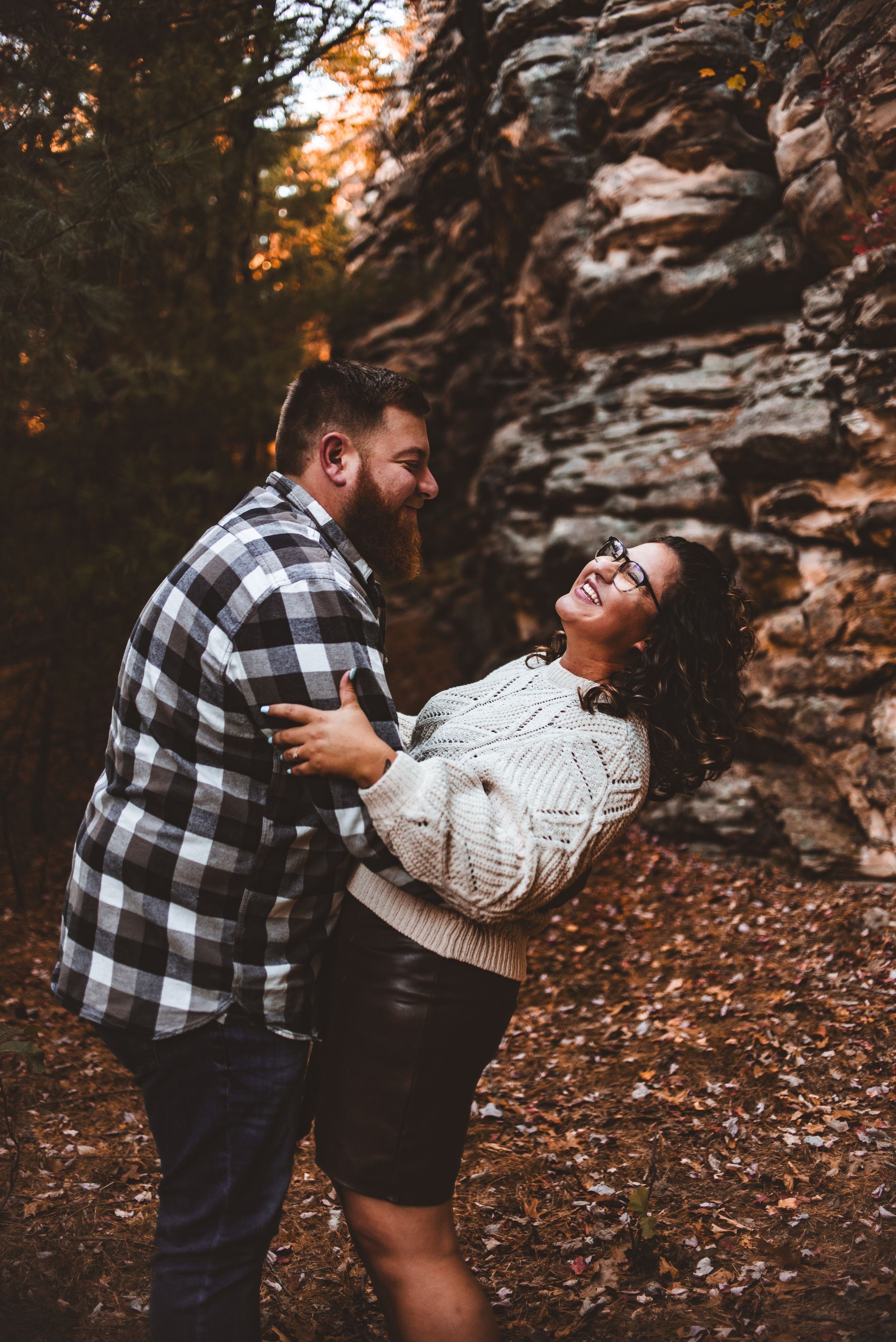Candid moment of laughter between a couple during their fall photoshoot by a rock formation.
