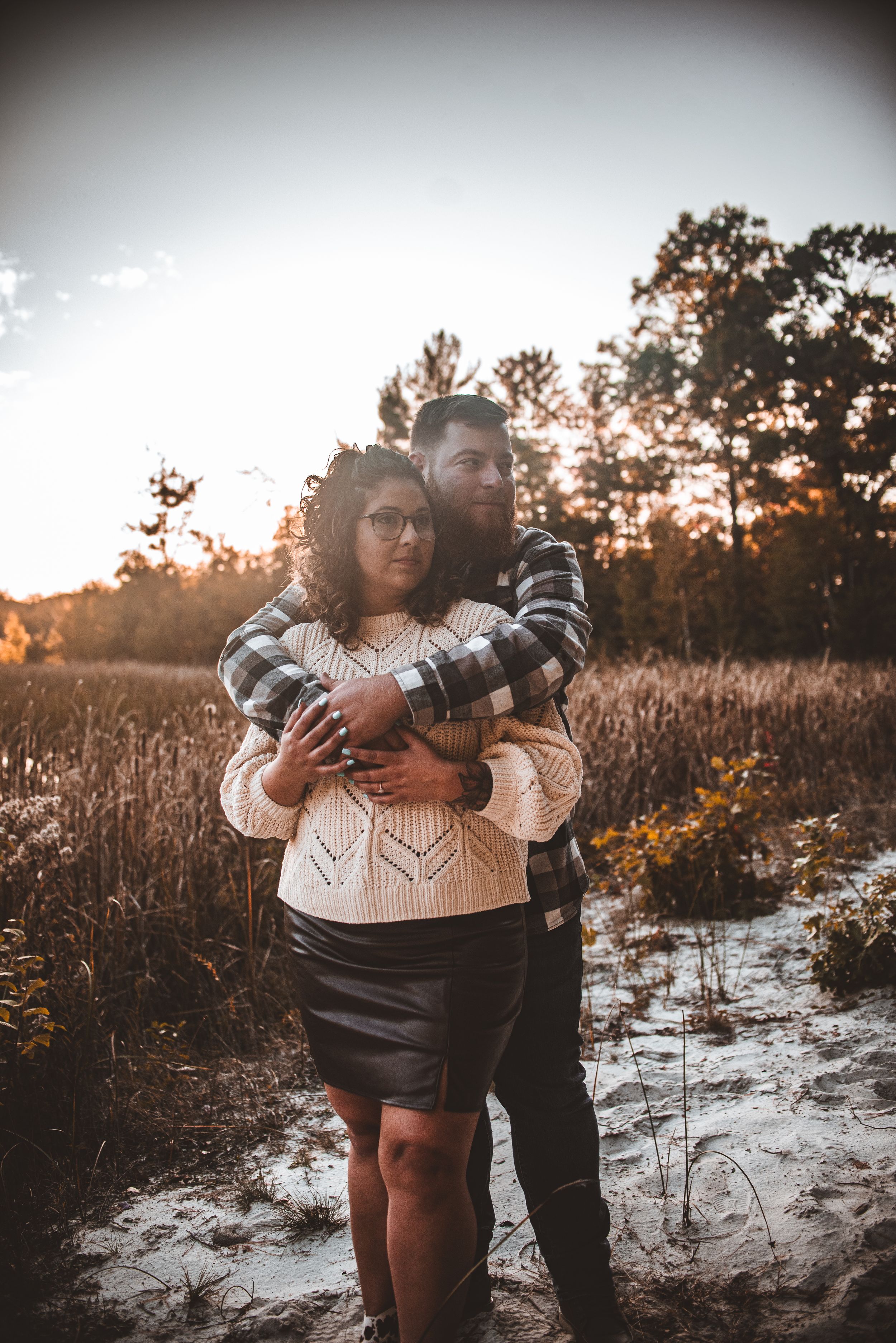A couple embraces in a winter landscape with tall grass and snow at sunset.
