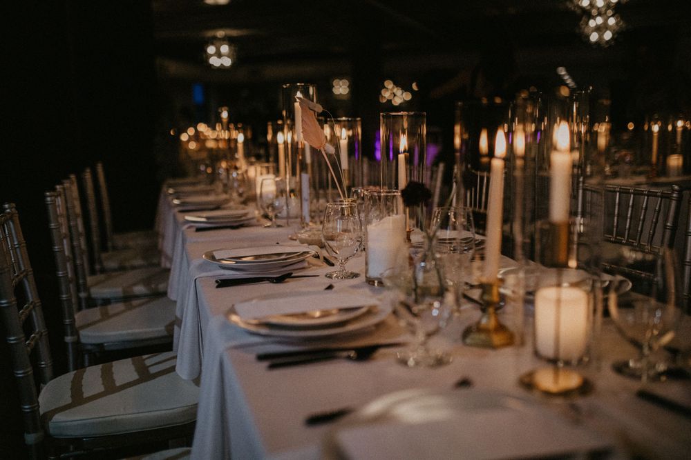 Elegant wedding reception tables decorated with white linens, candles and floral centerpieces in an indoor venue.