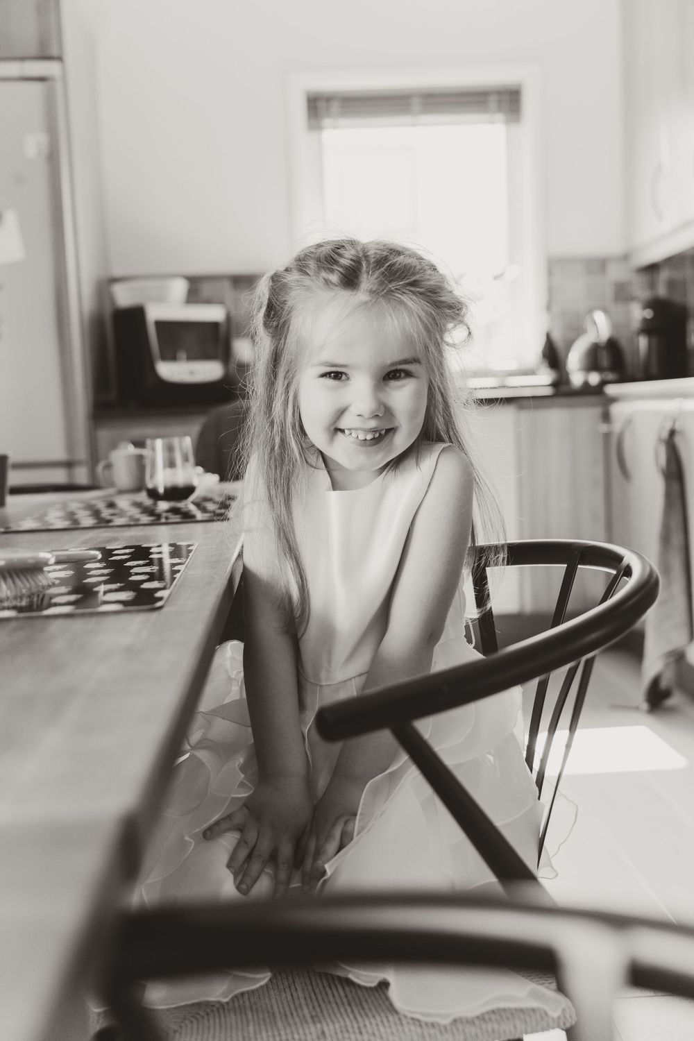Black and white portrait of a young child sitting at a kitchen table.