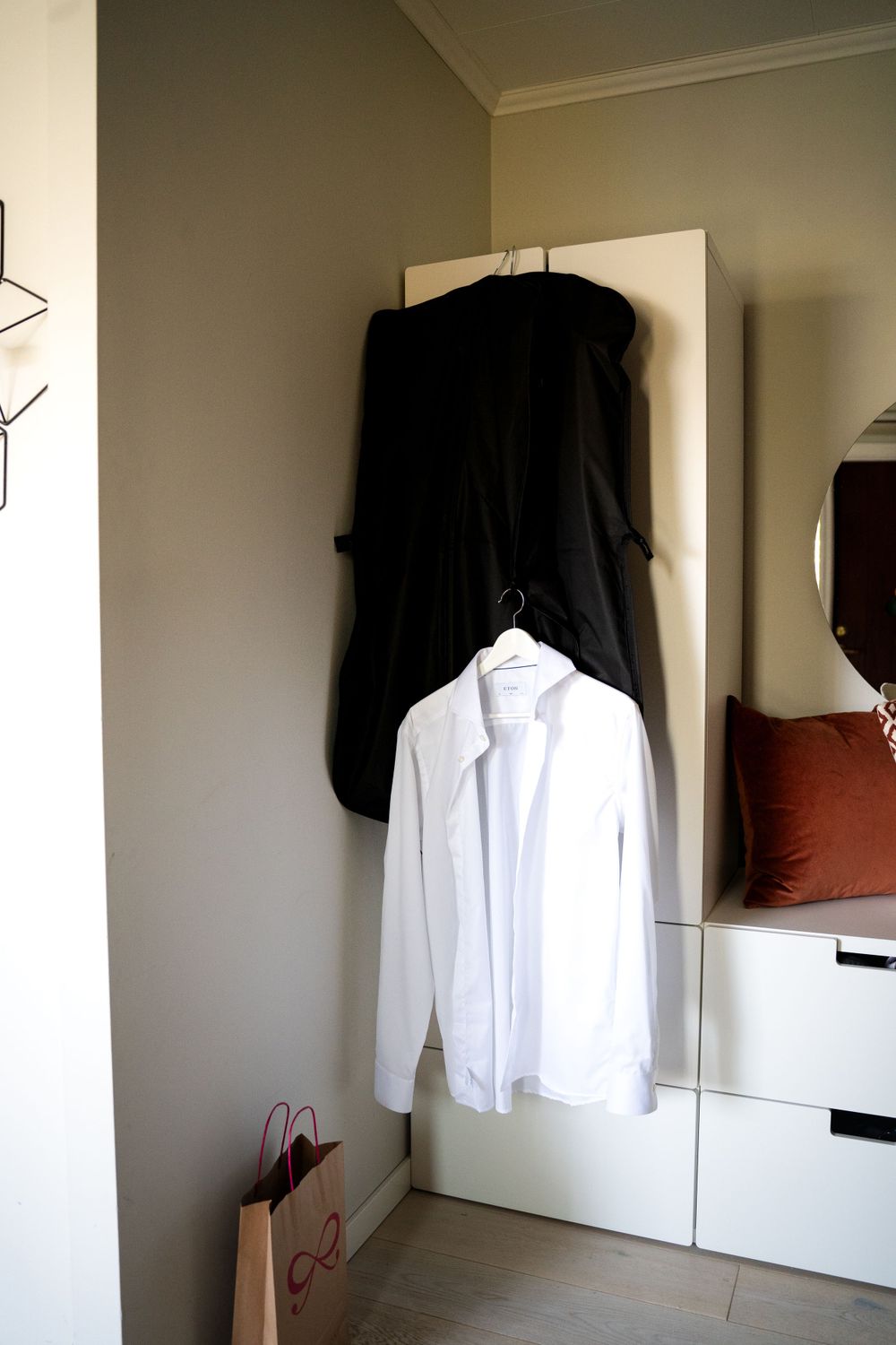 Wedding attire hanging on display - black suit and white dress shirt on white wall.