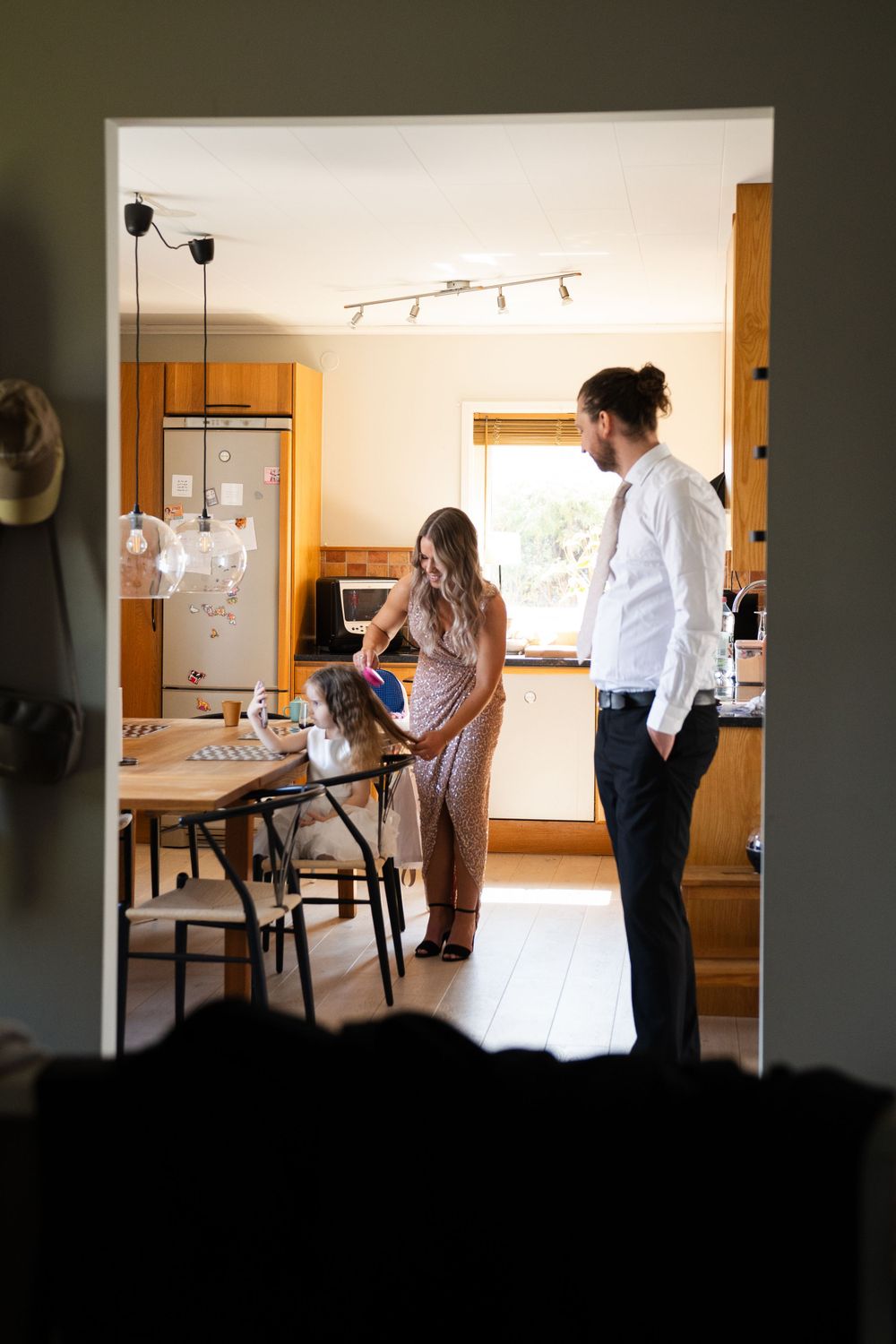 Intimate gathering in sunlit kitchen seen through doorframe.