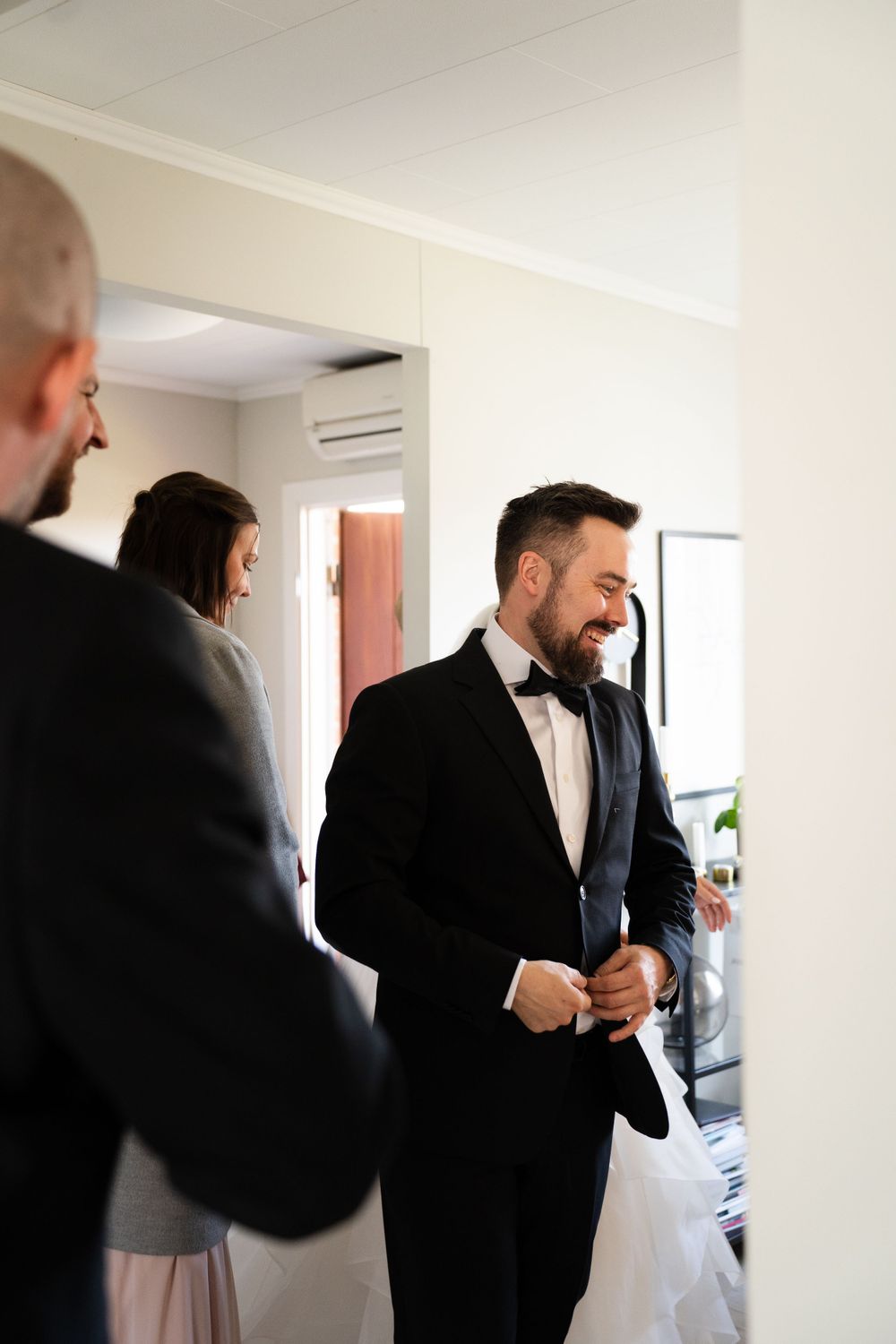 A groom in a black tuxedo laughs joyfully while getting ready for his wedding day.