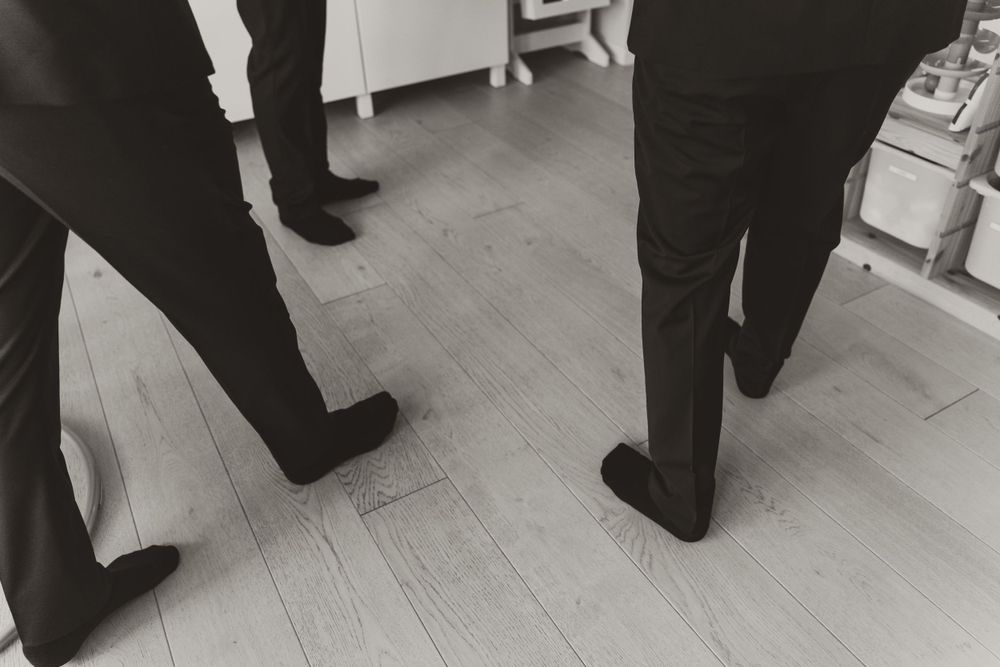 Black and white detail shot of formal shoes and suits on hardwood floor.