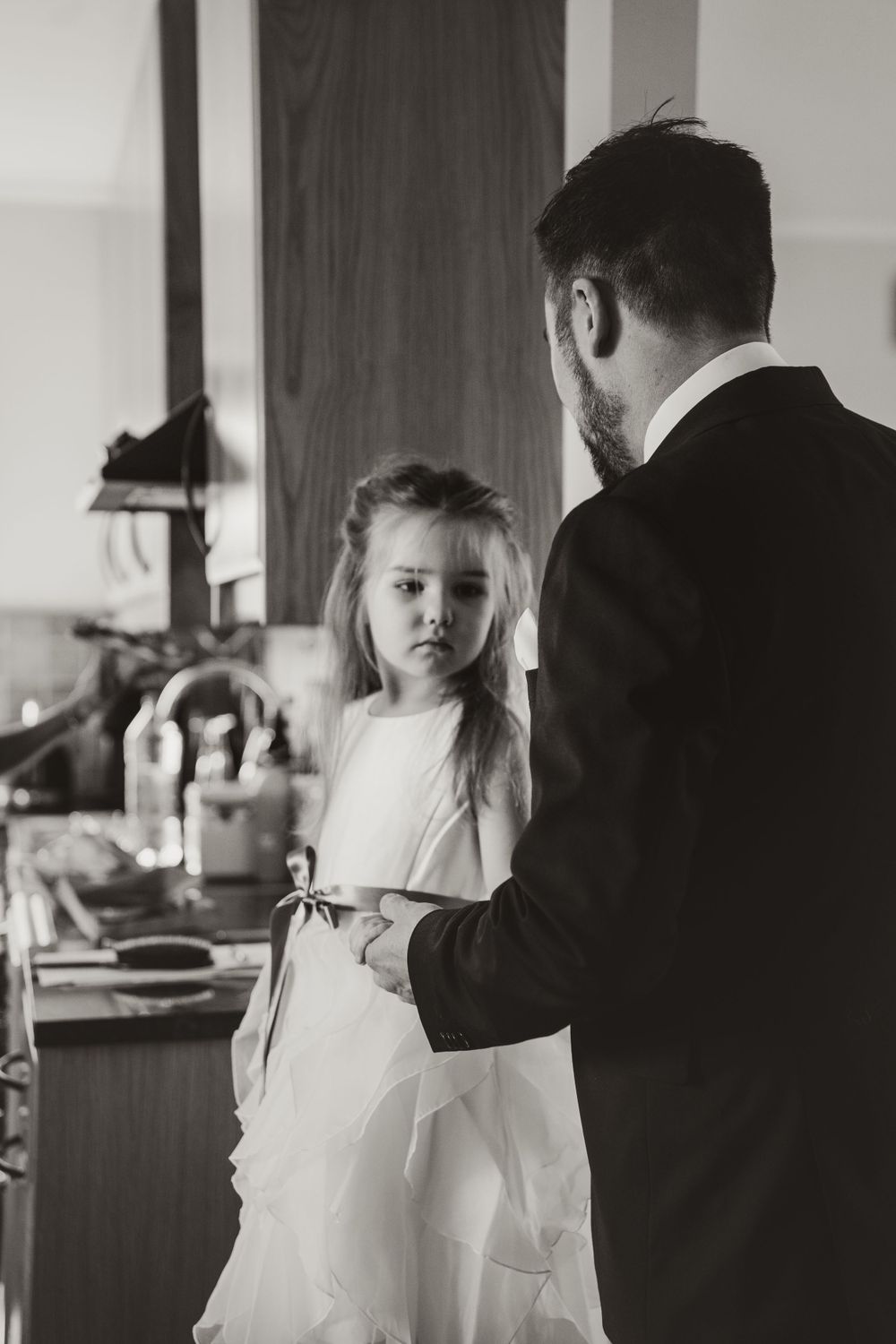 A touching moment between a flower girl in white dress and wedding party member.