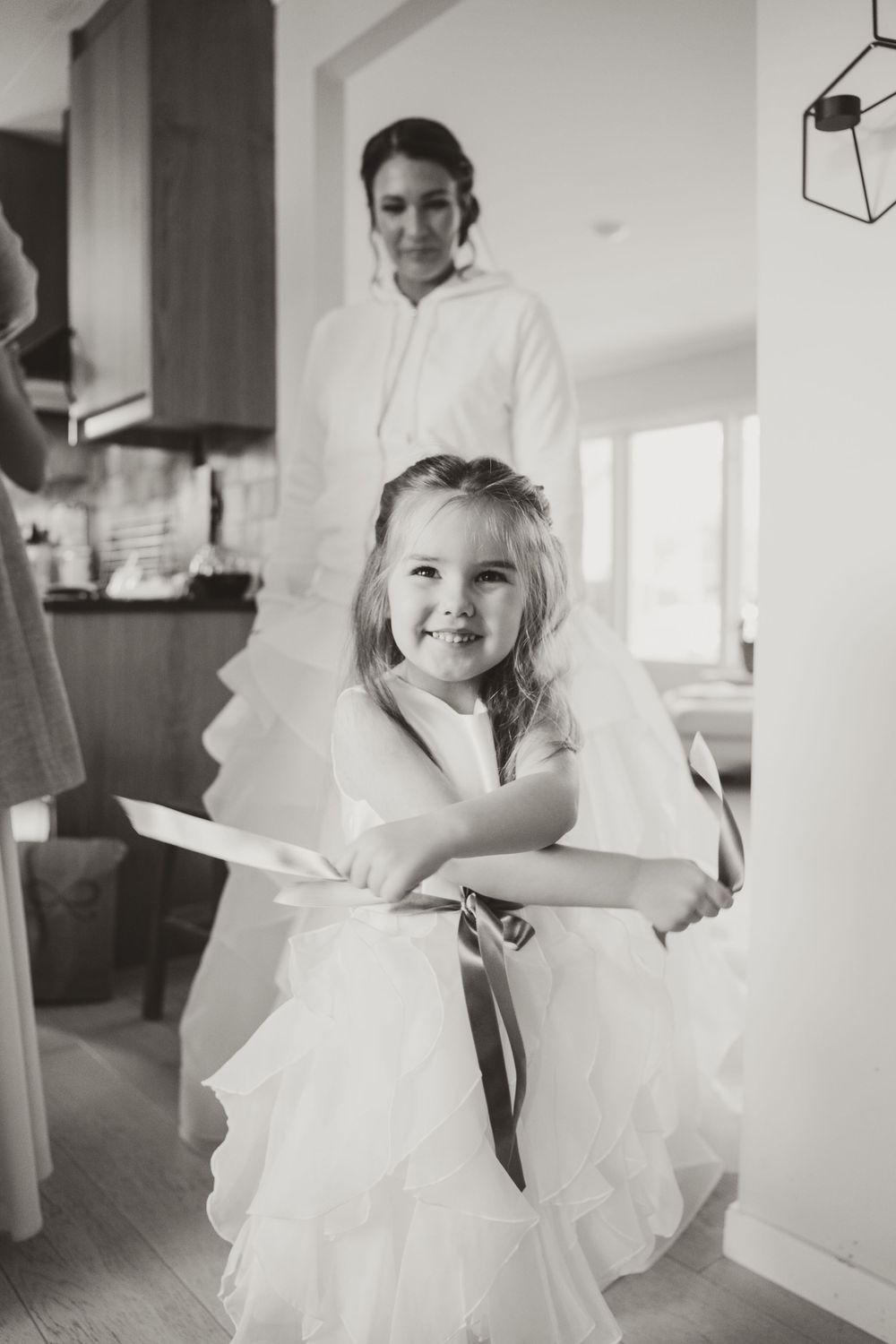 Young flower girl in white dress smiles brightly during wedding preparations.
