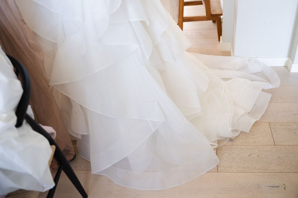 Close-up detail shot of flowing white wedding dress layers against light wooden flooring.