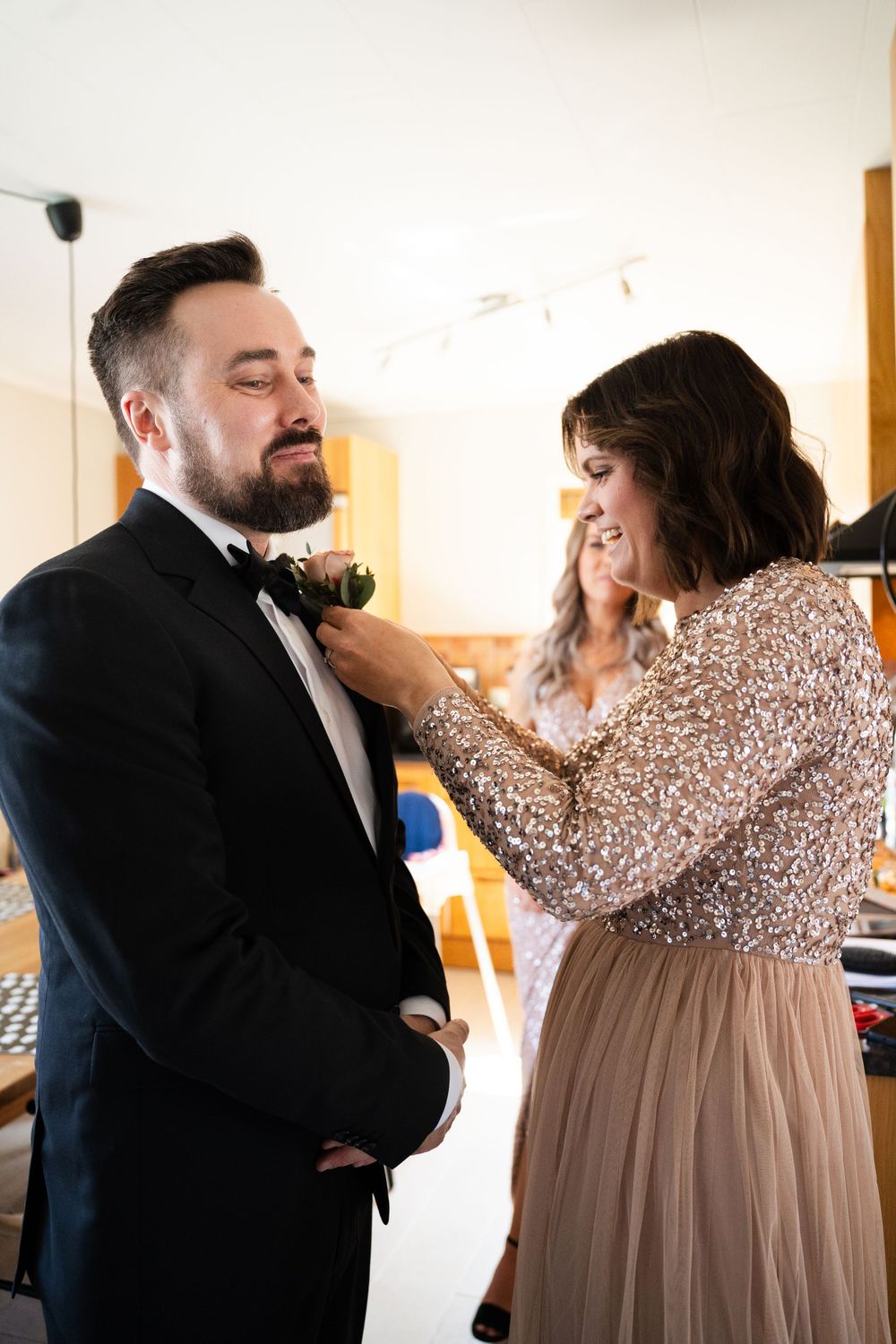 Wedding party member adjusts groom's boutonniere while both share a laugh.