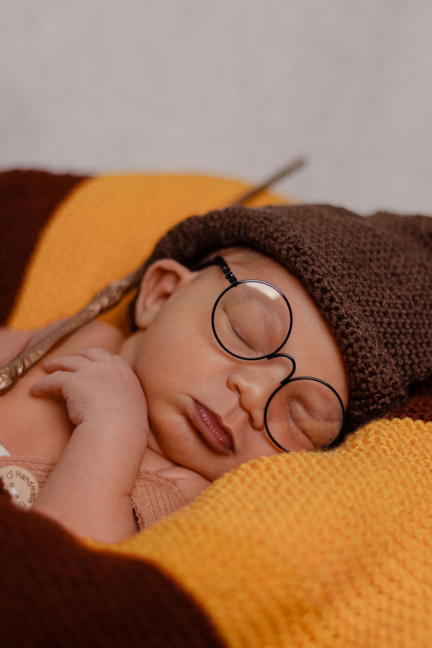 Baby sleeping peacefully wearing round glasses and brown knit hat on orange background.