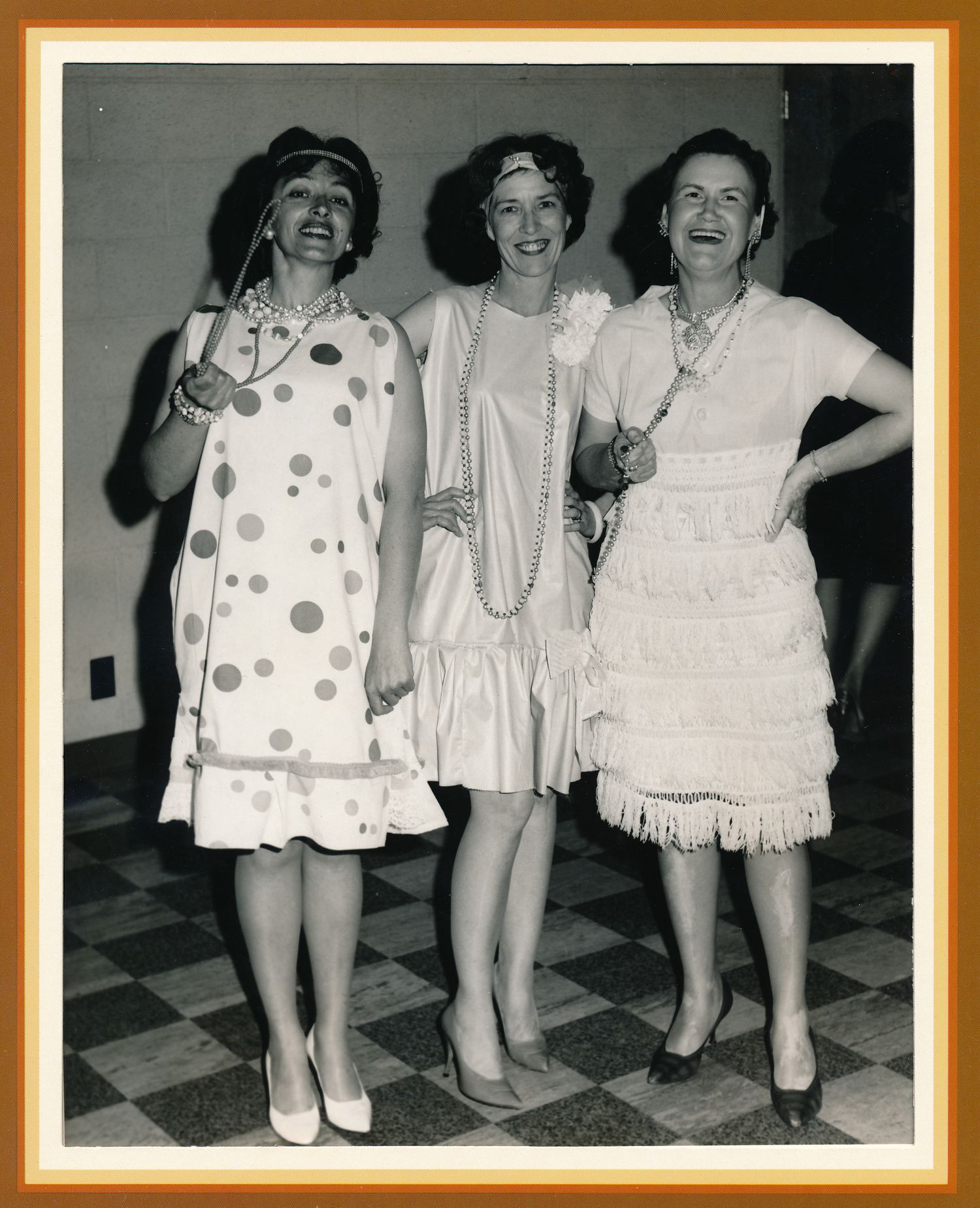 Three women in the 50s dressing up in 20s style clothing at a dance wearing pearls and smiling big