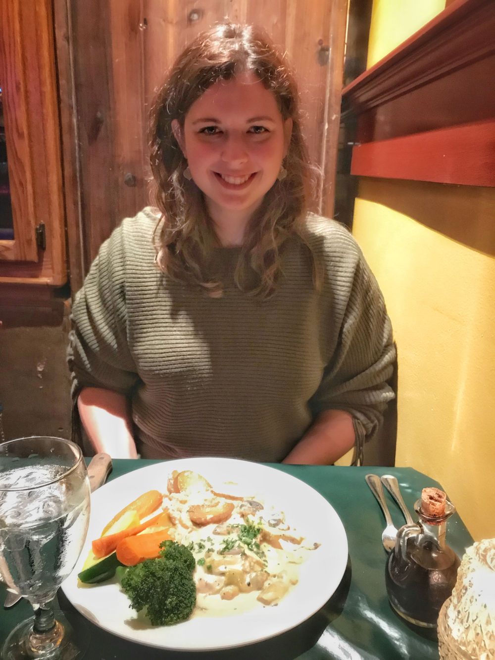 A diner sits at a rustic restaurant table with a plated meal of vegetables.