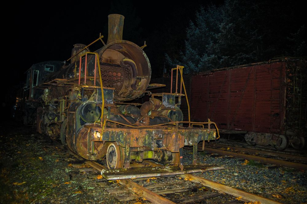 Rusty vintage steam locomotive abandoned on railroad tracks at night.