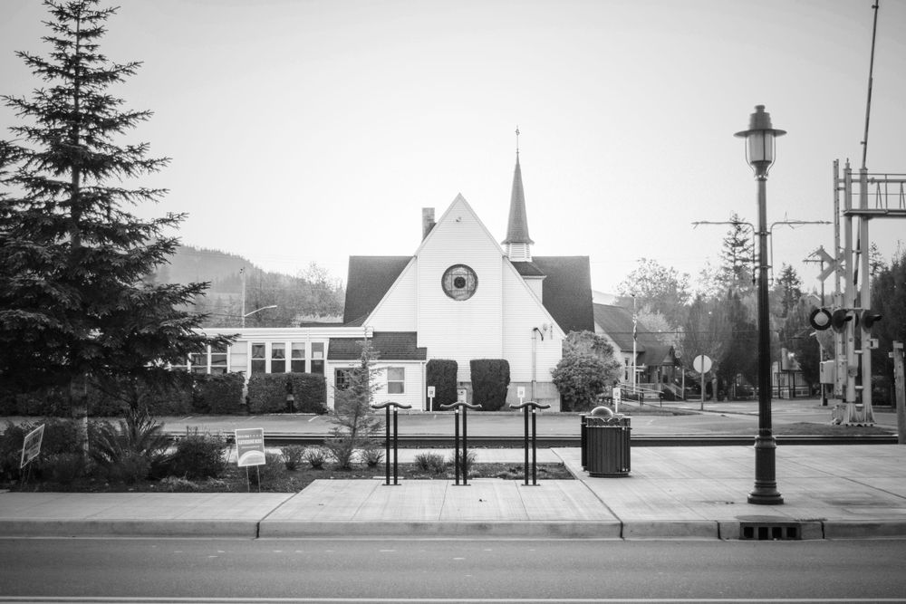 Black and white photo of a small church with spire and lamppost in foreground.