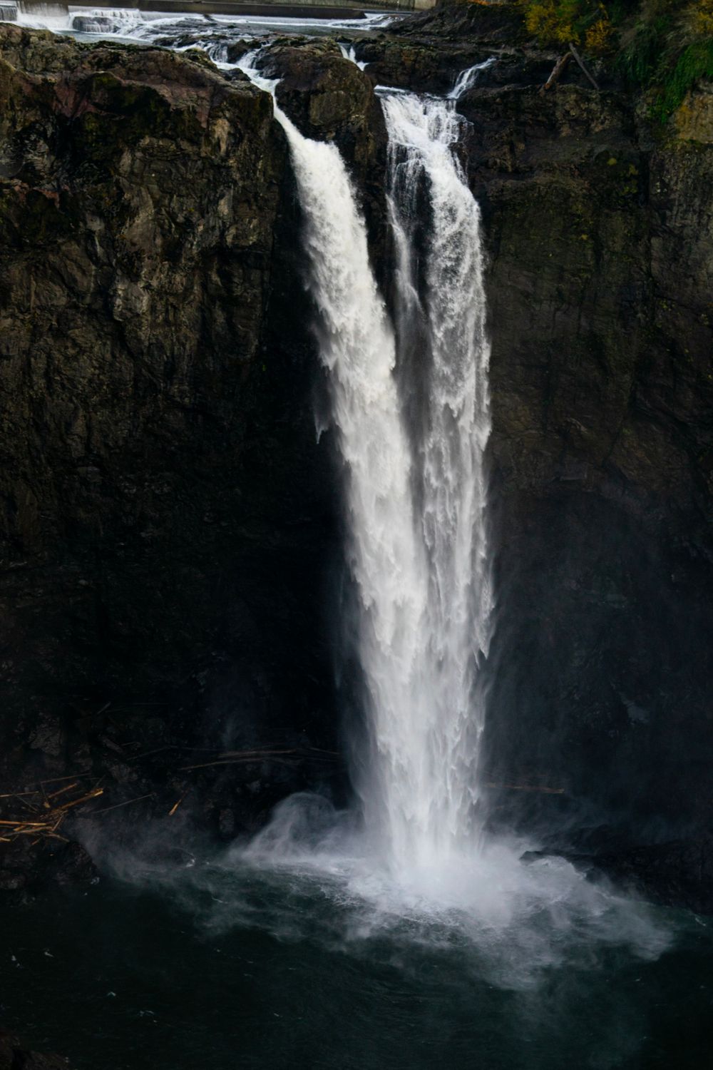 A powerful waterfall cascades down a rocky cliff face into a misty pool below.
