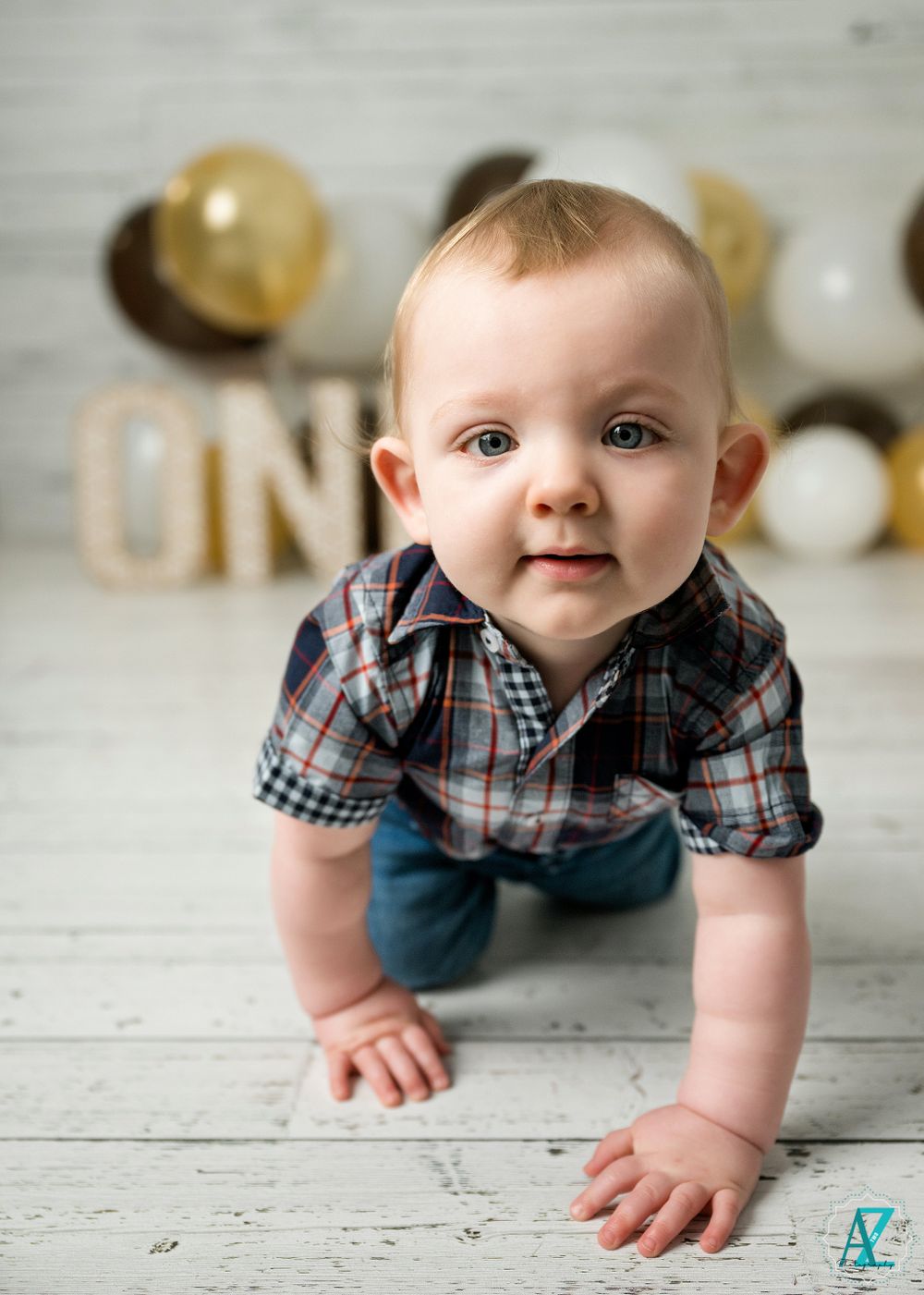 A baby in plaid crawls forward during a first birthday photoshoot with balloons.