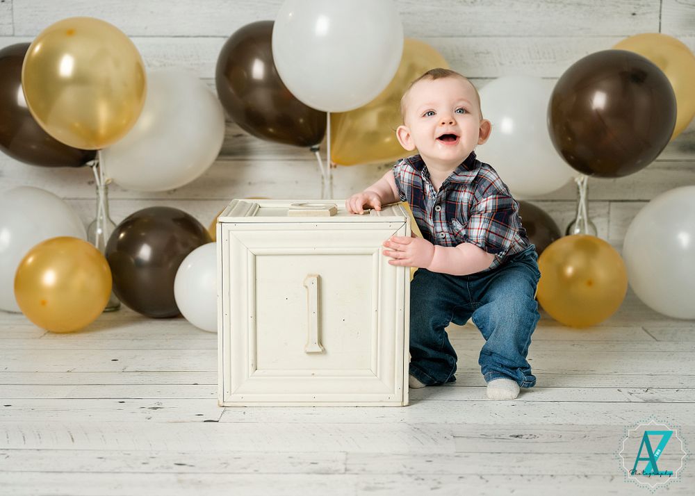 First birthday photo setup with brown and gold balloons and white wooden number one prop against shiplap wall.