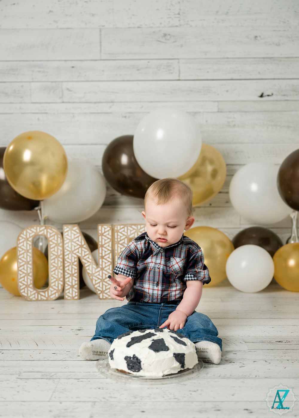 Festive birthday scene with gold and brown balloons, ONE letters, and cow print cushion on wooden floor.