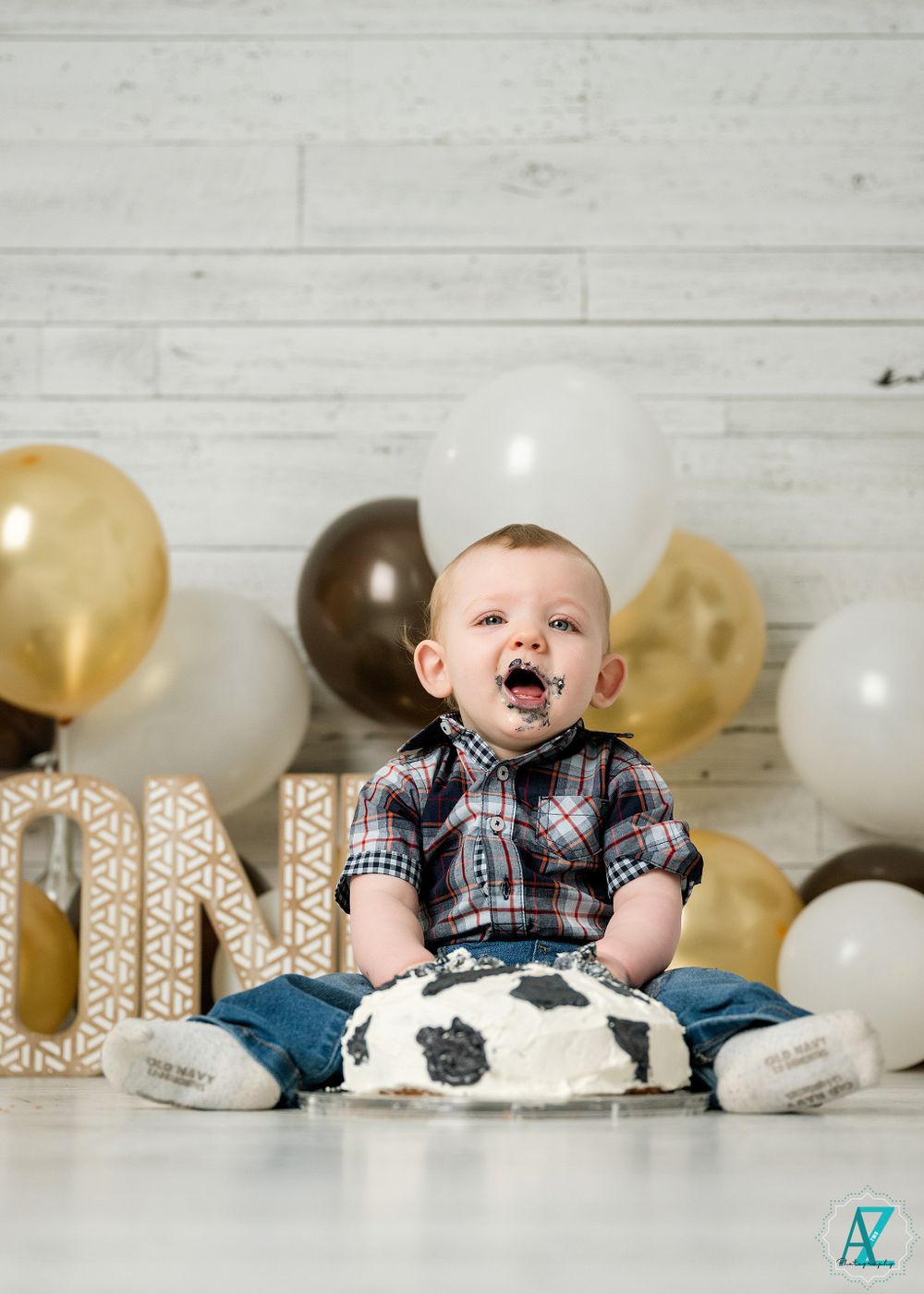 First birthday scene with cow print cake smash setup and gold letter decorations.