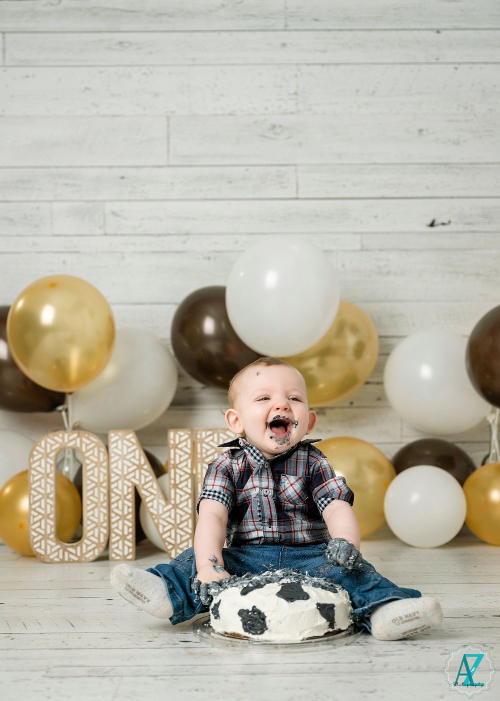 Celebratory birthday setup with balloon decorations and cow print cake against white wooden wall.