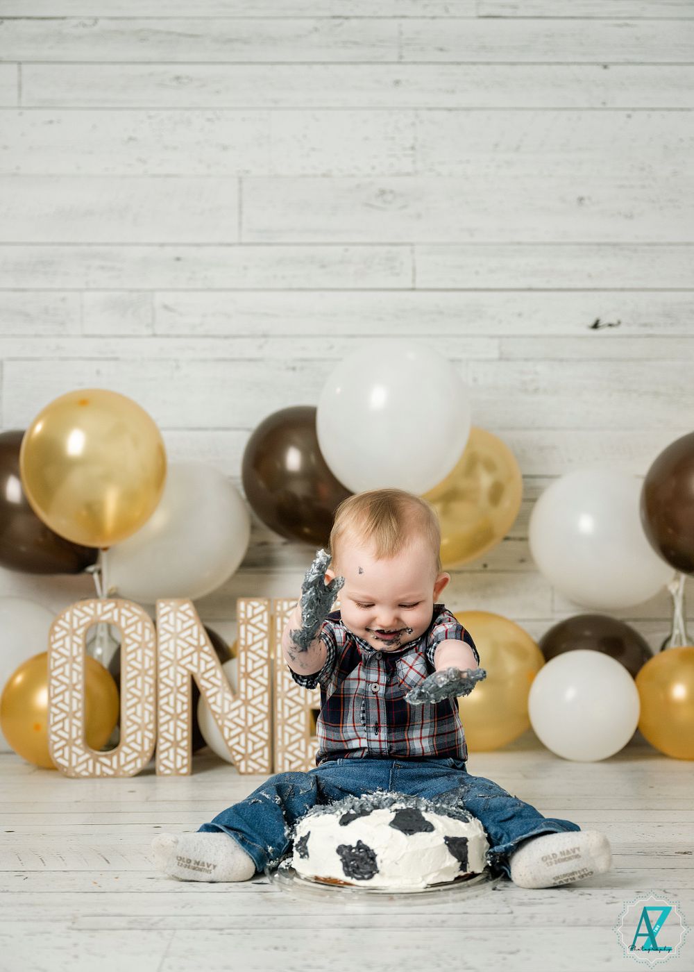 First birthday photo featuring decorative ONE letters and brown and gold balloon arrangement.