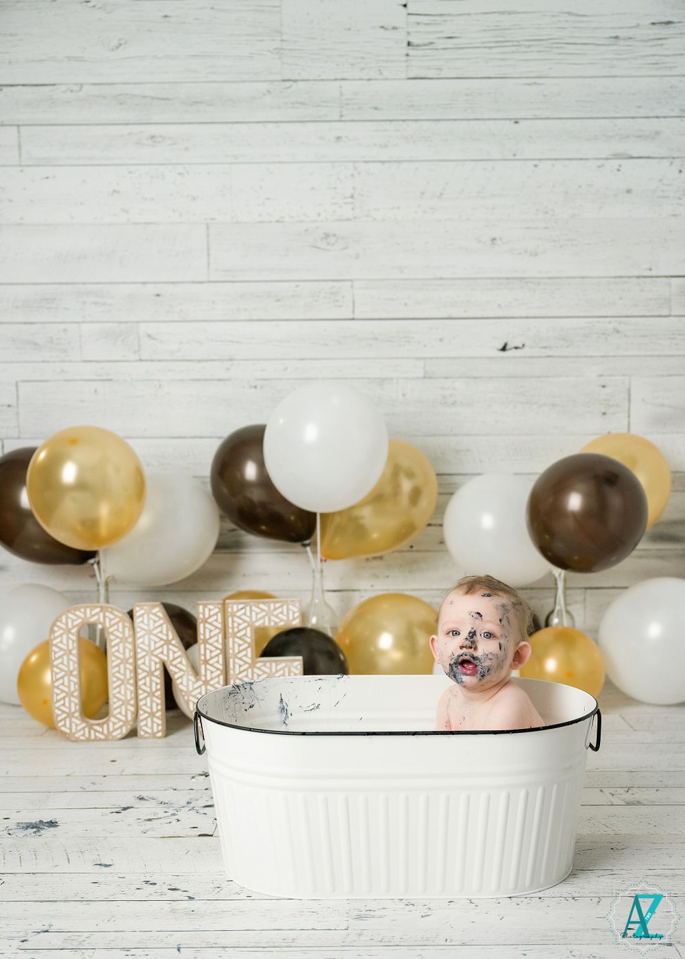 Cake smash birthday photo with white washtub and gold balloon decorations against shiplap wall.