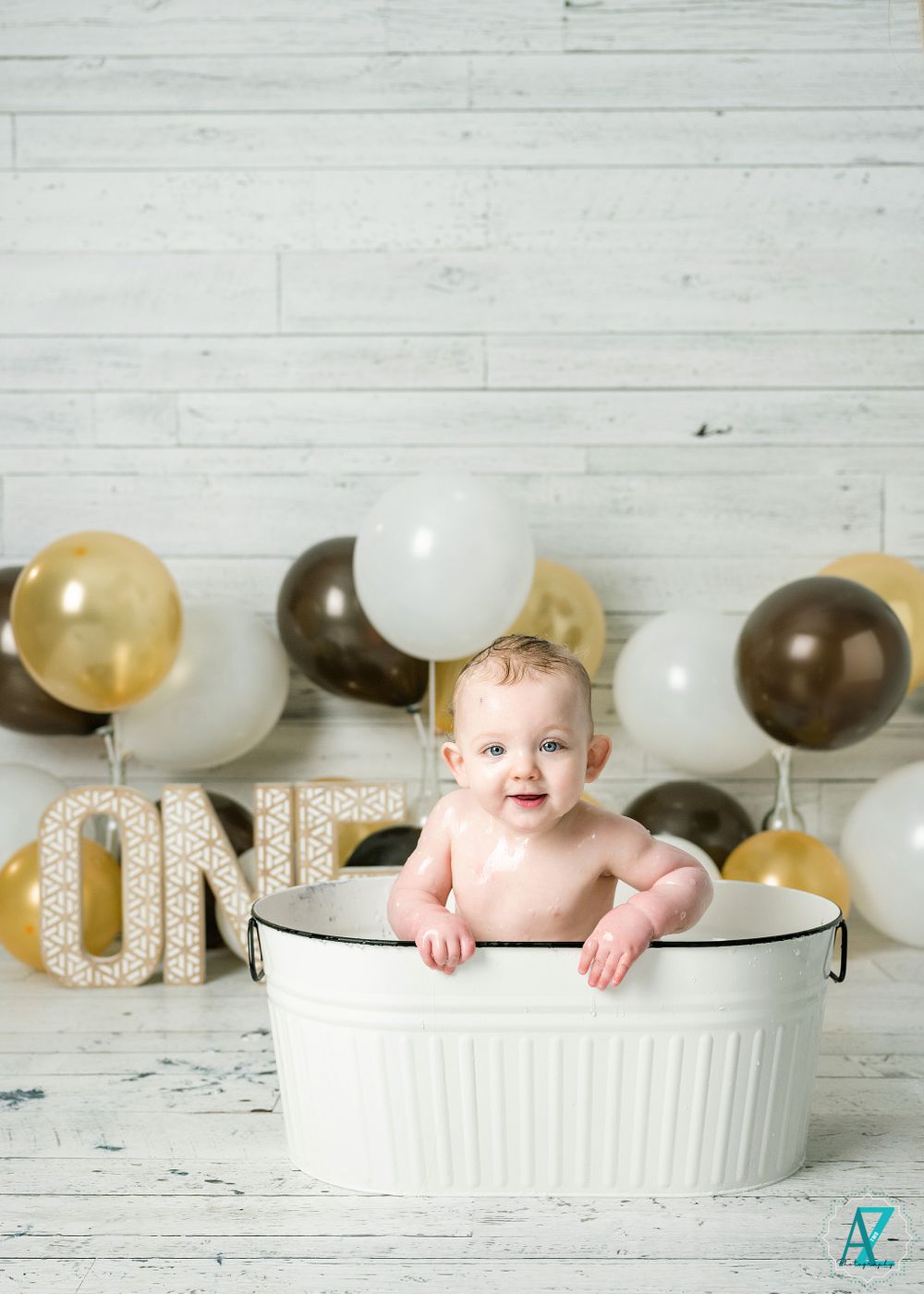 First birthday photo with white vintage washtub and gold and brown balloon backdrop.