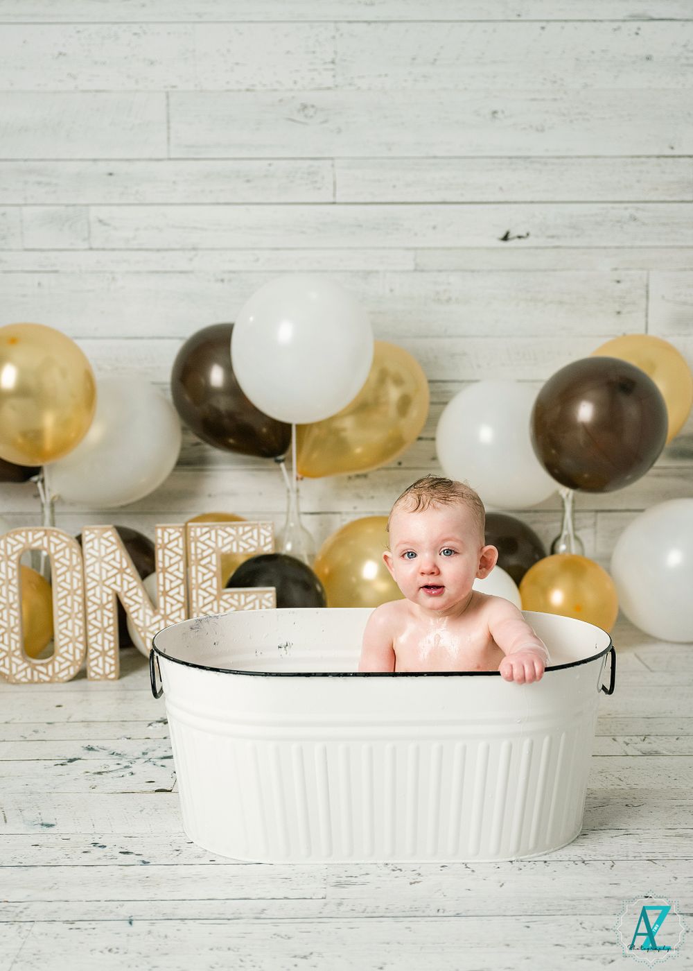 First birthday setup with white washtub and gold and brown balloon arrangement against wooden wall.