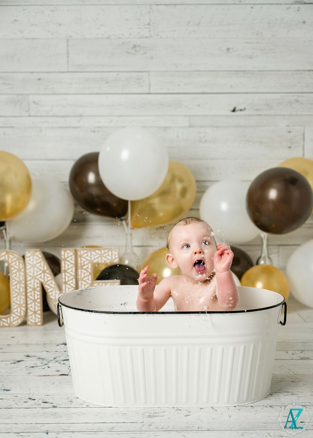 A festive one-year birthday scene with brown and gold balloons and a white basin against shiplap walls.