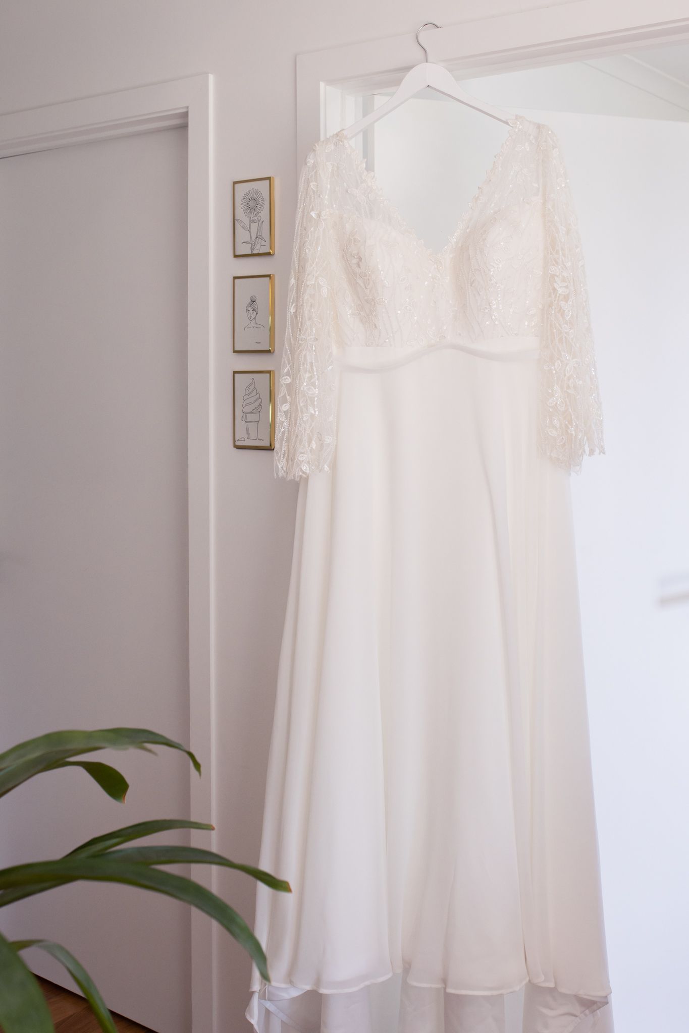 An elegant white lace wedding dress with long sleeves hanging against a light gray wall.
