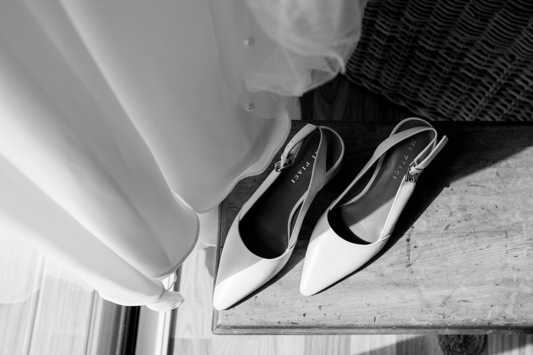 Artistic black and white photo of white bridal shoes next to flowing fabric.