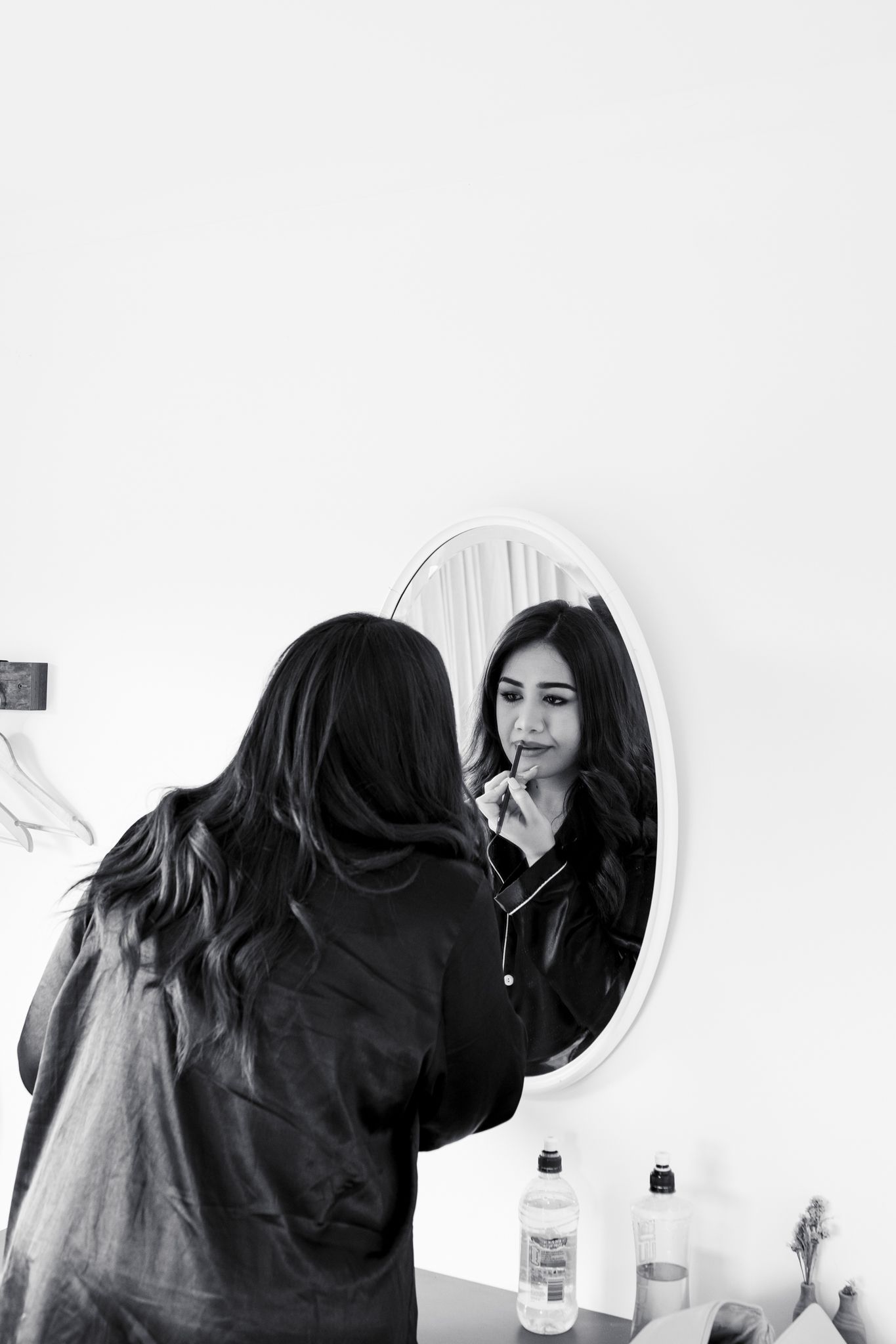 A person applying makeup in front of an oval mirror during wedding preparations.