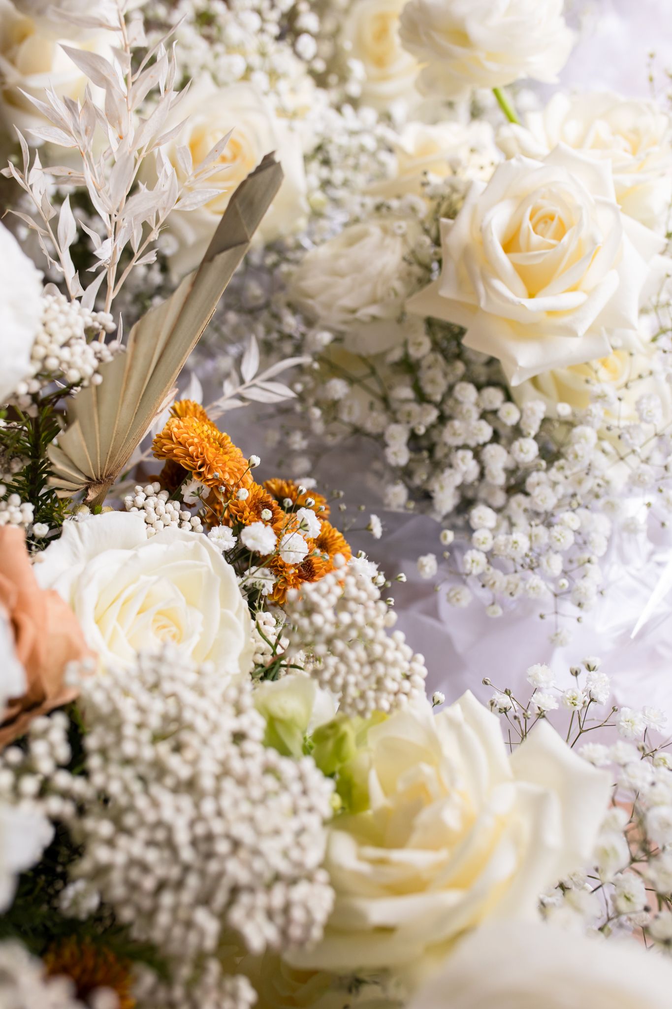 Close-up of white roses and baby's breath bouquet with orange floral accents.