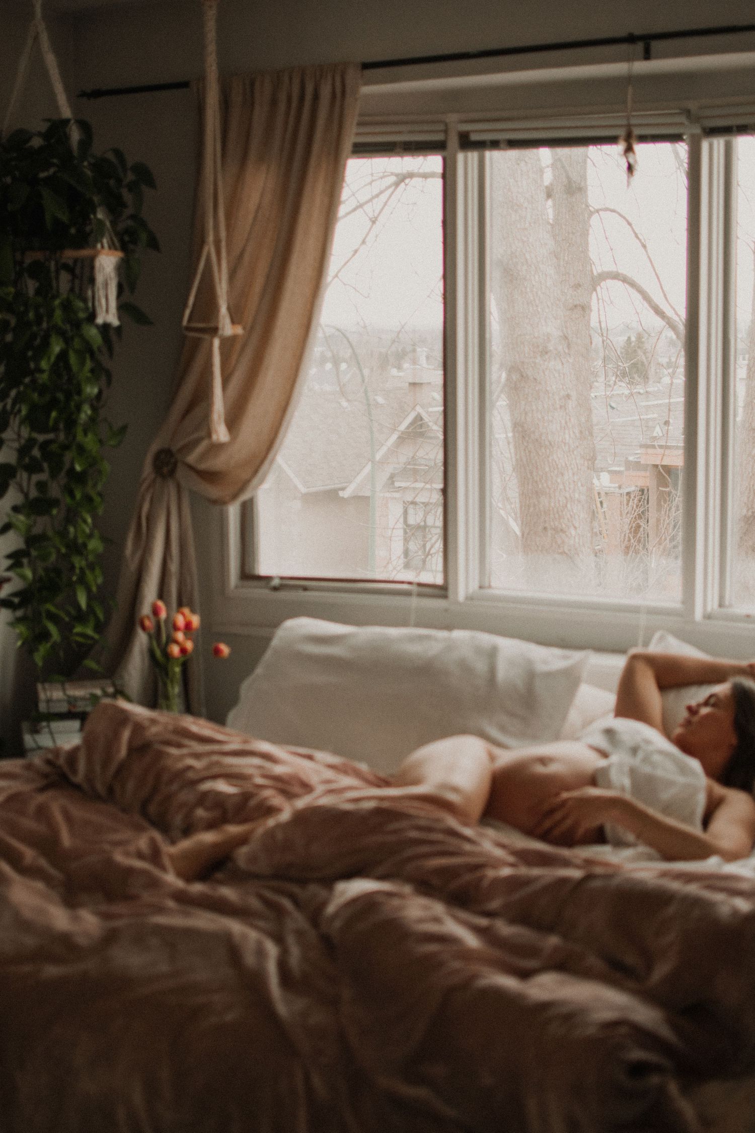 Cozy bedroom interior with unmade bed, curtains, and winter view through window.