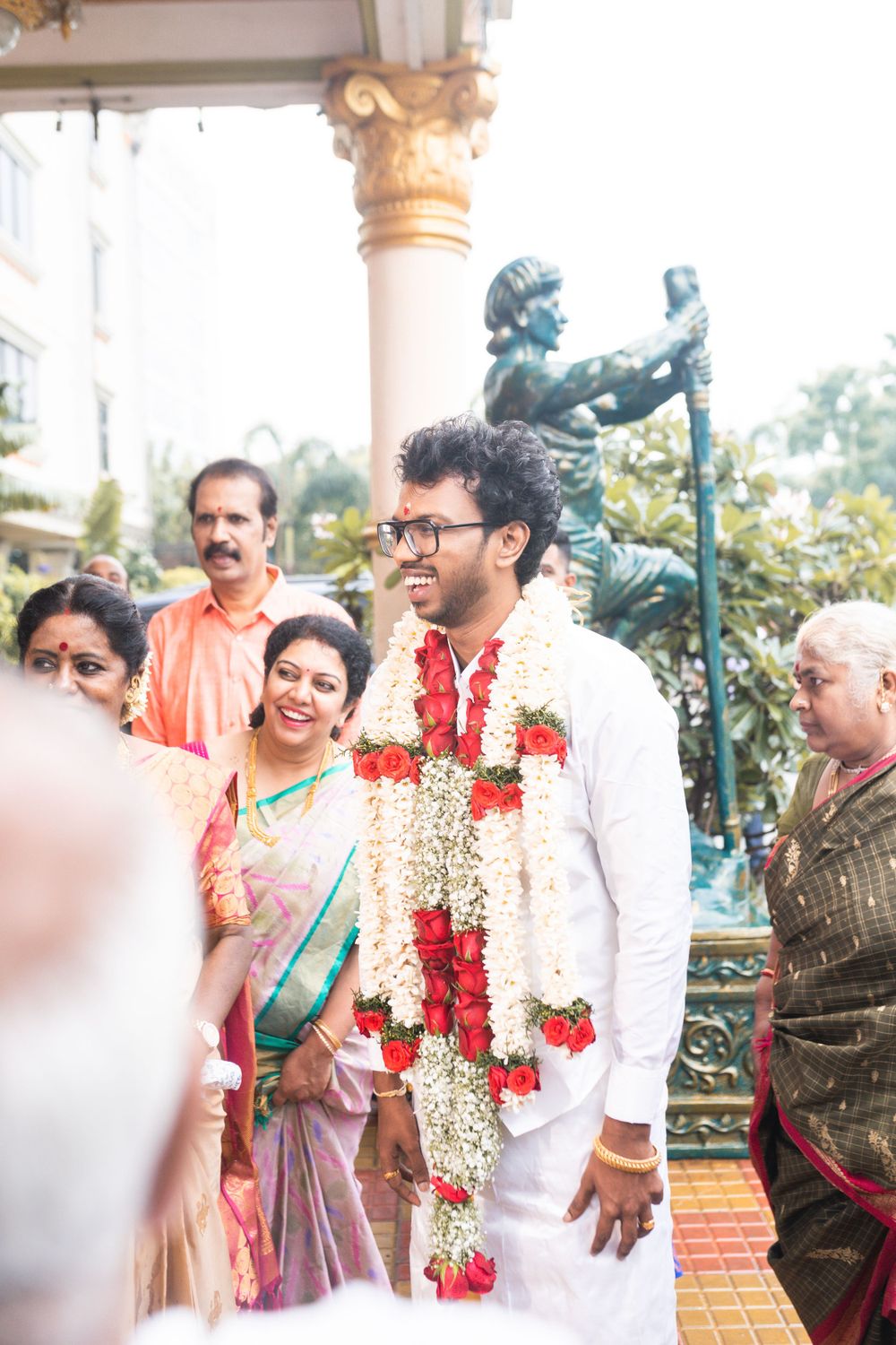 A traditional South Indian wedding ceremony with guests gathered around an ornate pillar and decorative statue.