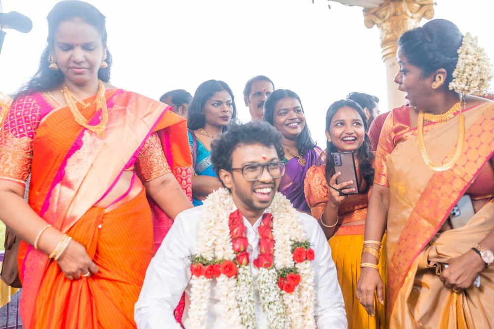 A festive gathering of wedding guests in bright orange and red saris celebrating with laughter.