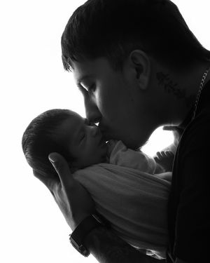 Black and white silhouette of father gently kissing his swaddled newborn baby.