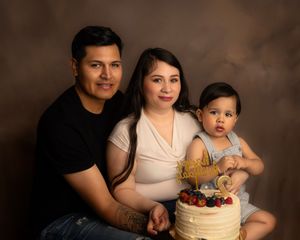 Family portrait with parents and baby celebrating first birthday with a decorated cake in a studio setting.